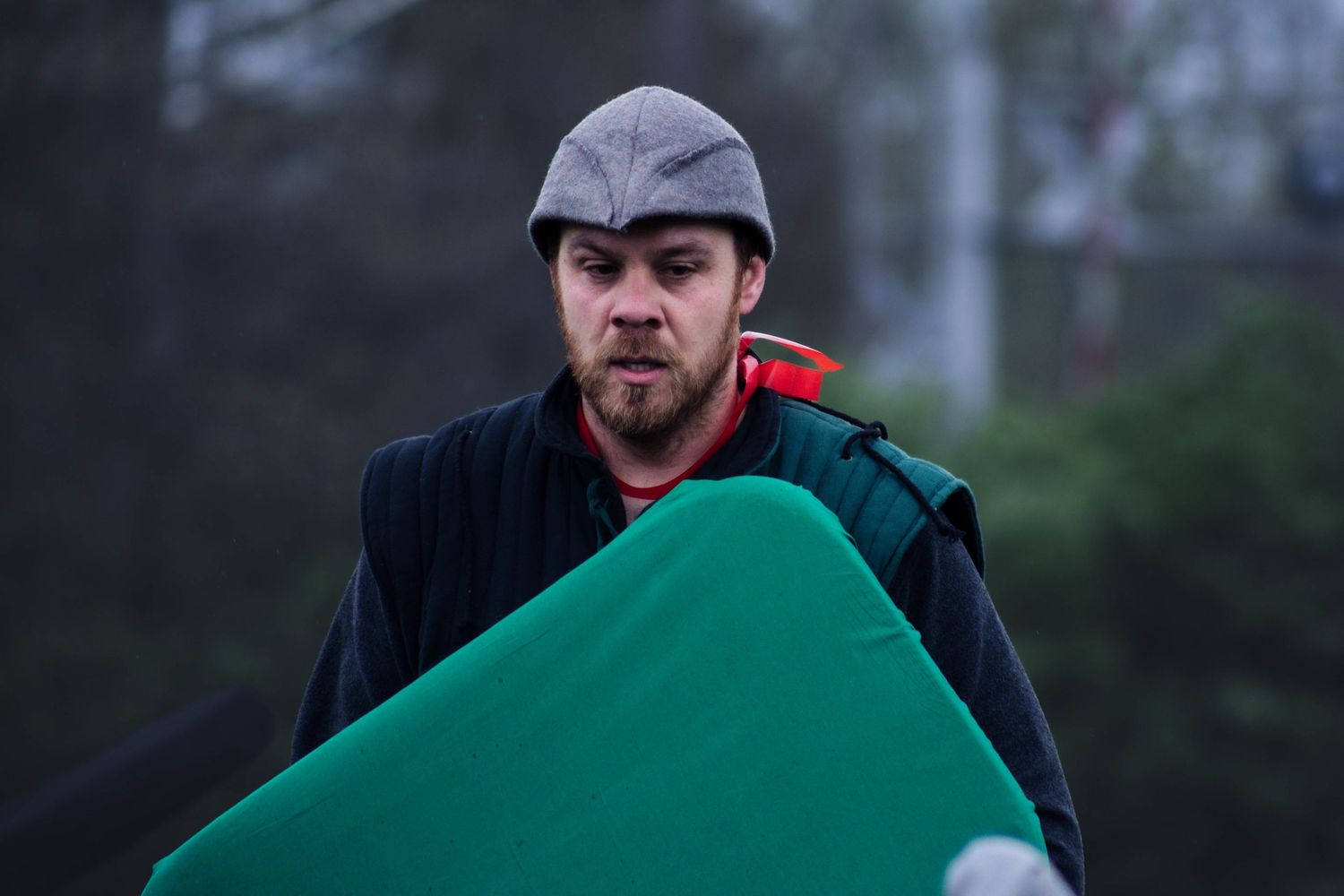 People carrying large green padded equipment outdoors.
