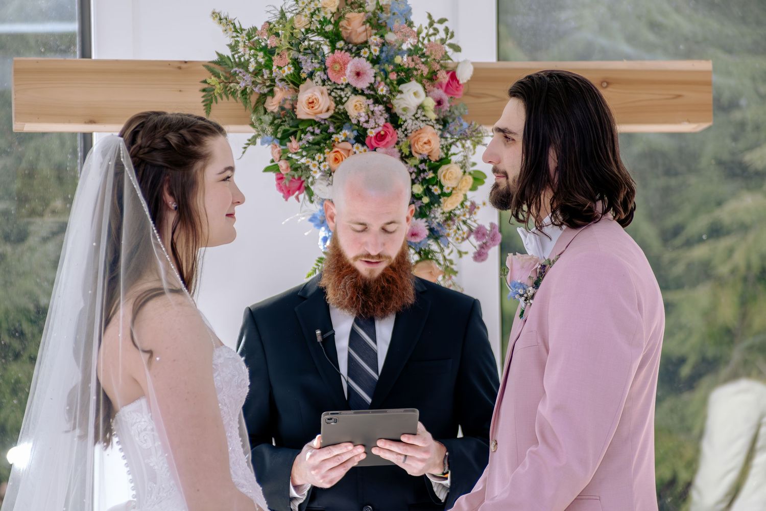 Bride and groom exchange vows before officiant at floral arch wedding ceremony.
