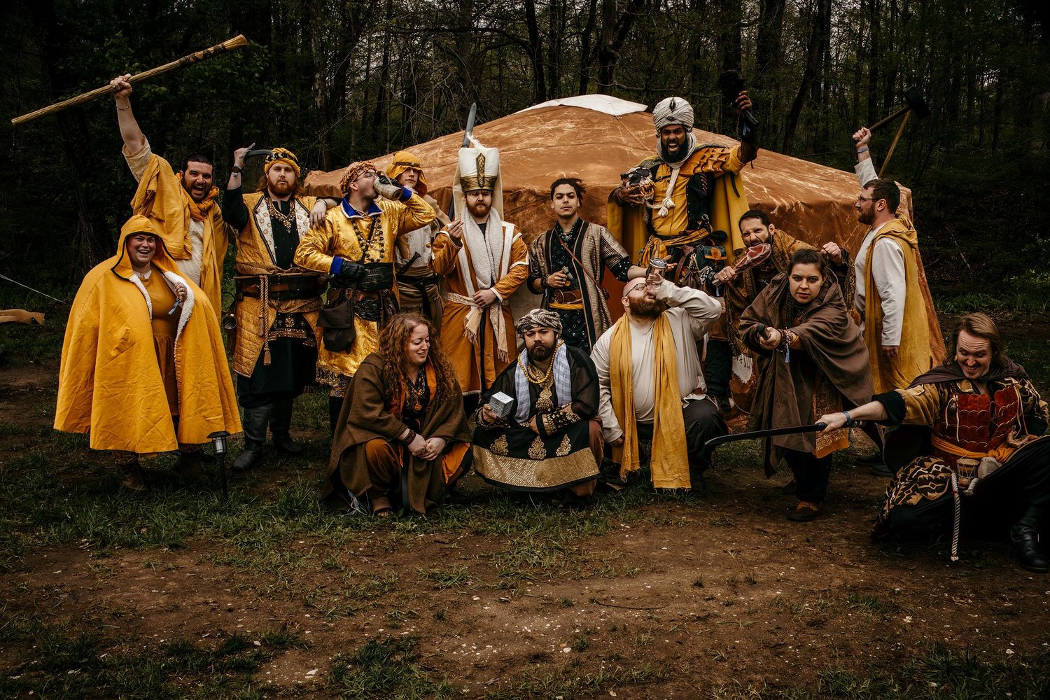 Group of medieval costumed performers posing in forest setting with golden cloaks and period costumes.