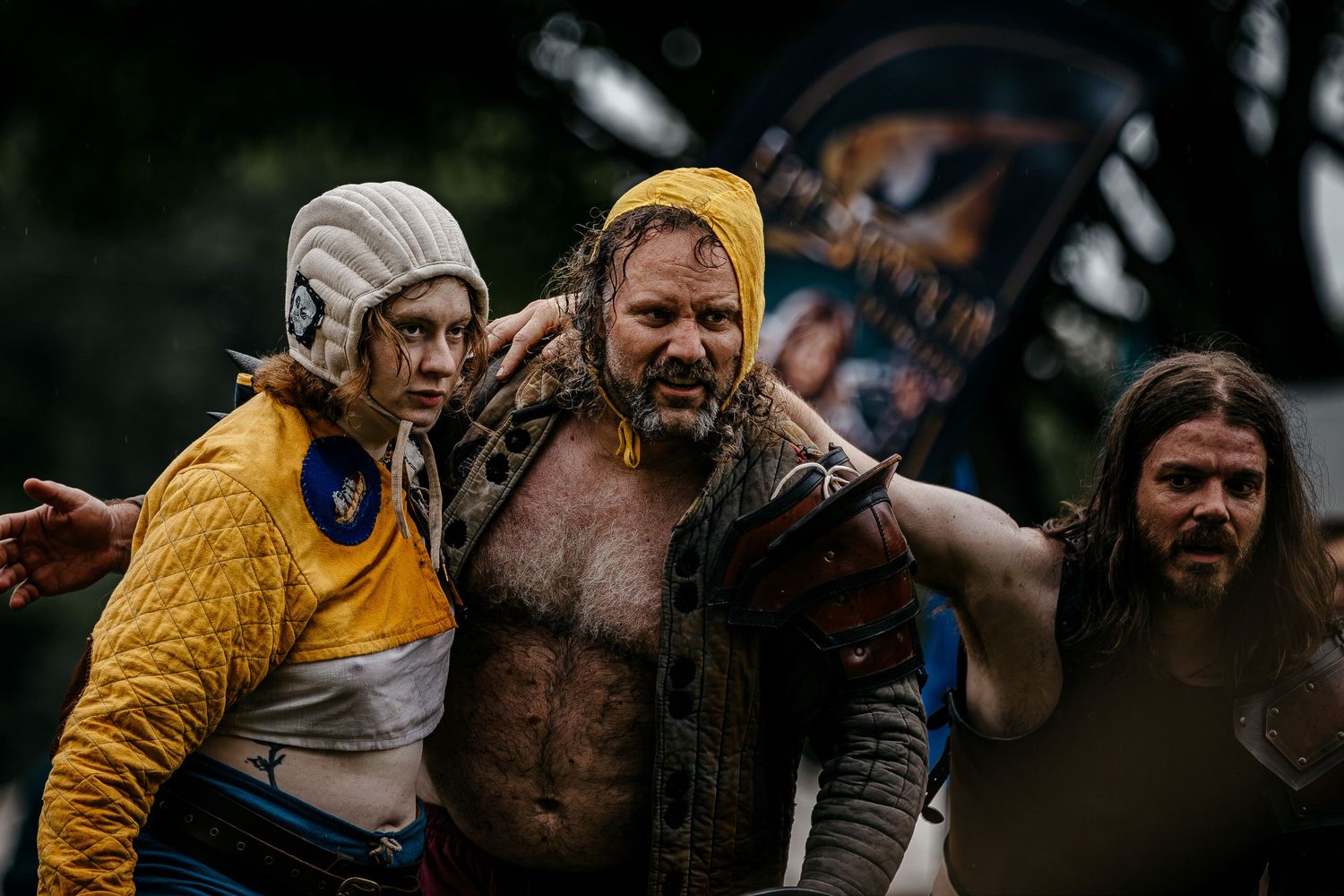 Three people in medieval fantasy costumes at an outdoor festival, featuring elaborate warrior and peasant attire.
