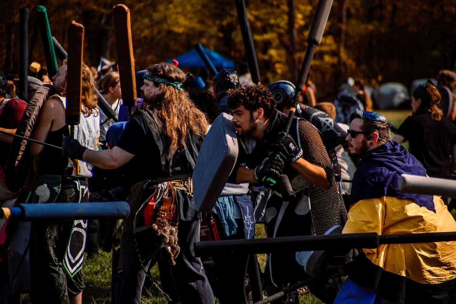 A large crowd of spectators sits on a grassy hill watching an outdoor event in the sunshine.