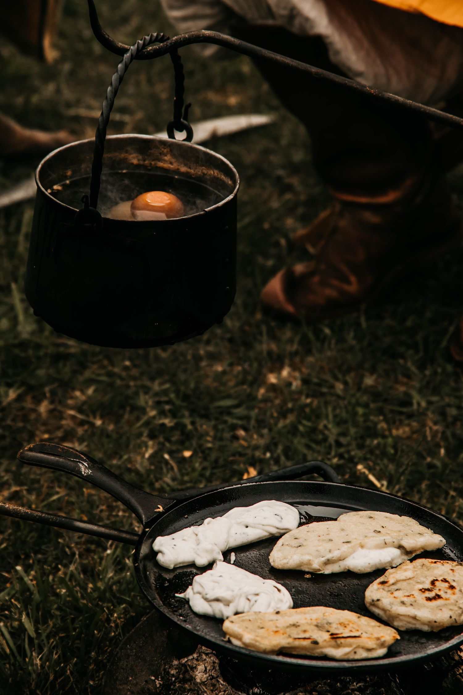 A cast iron pan with grilled flatbread cooking over a campfire in dark moody lighting.