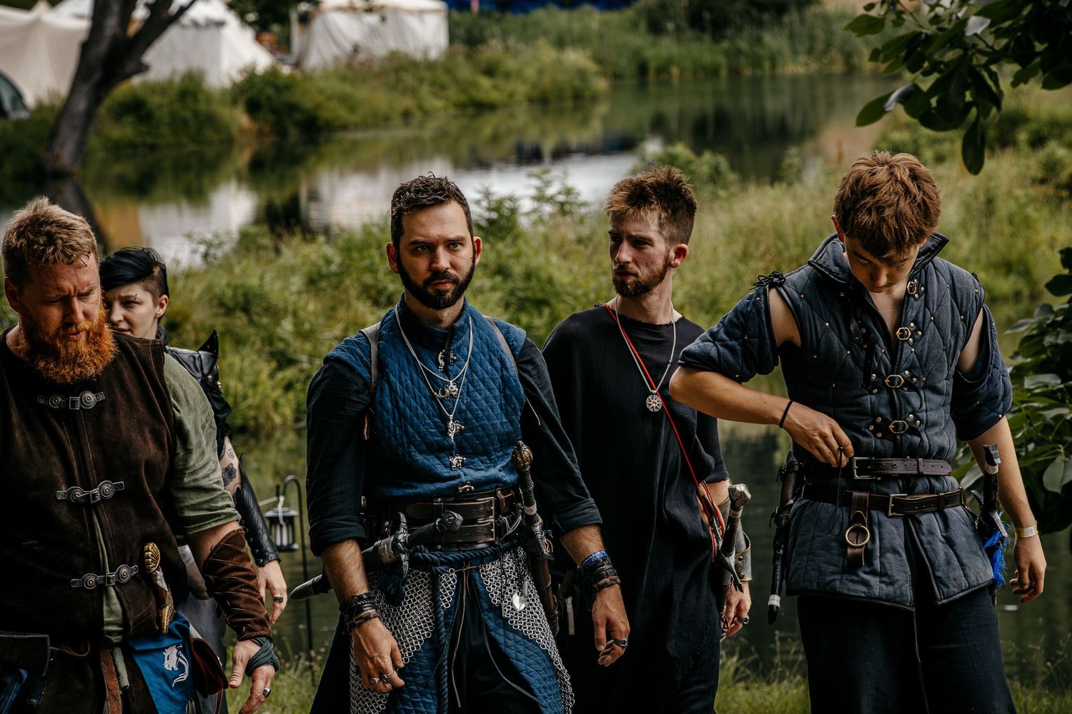 Group of men dressed in medieval Viking costumes at an outdoor historical reenactment event near a river.