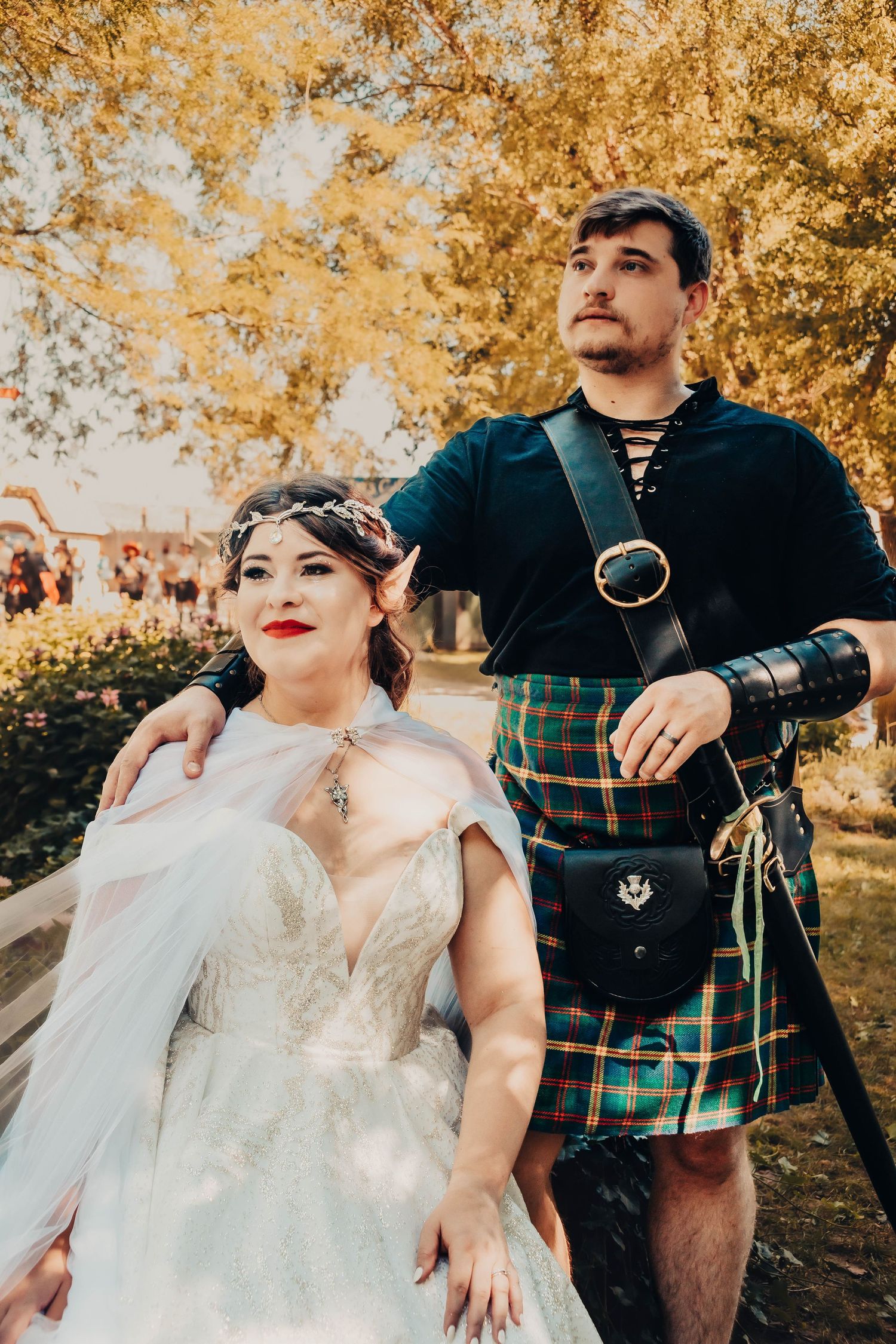Couple in wedding attire poses outdoors among autumn trees with golden foliage creating a romantic fall atmosphere.