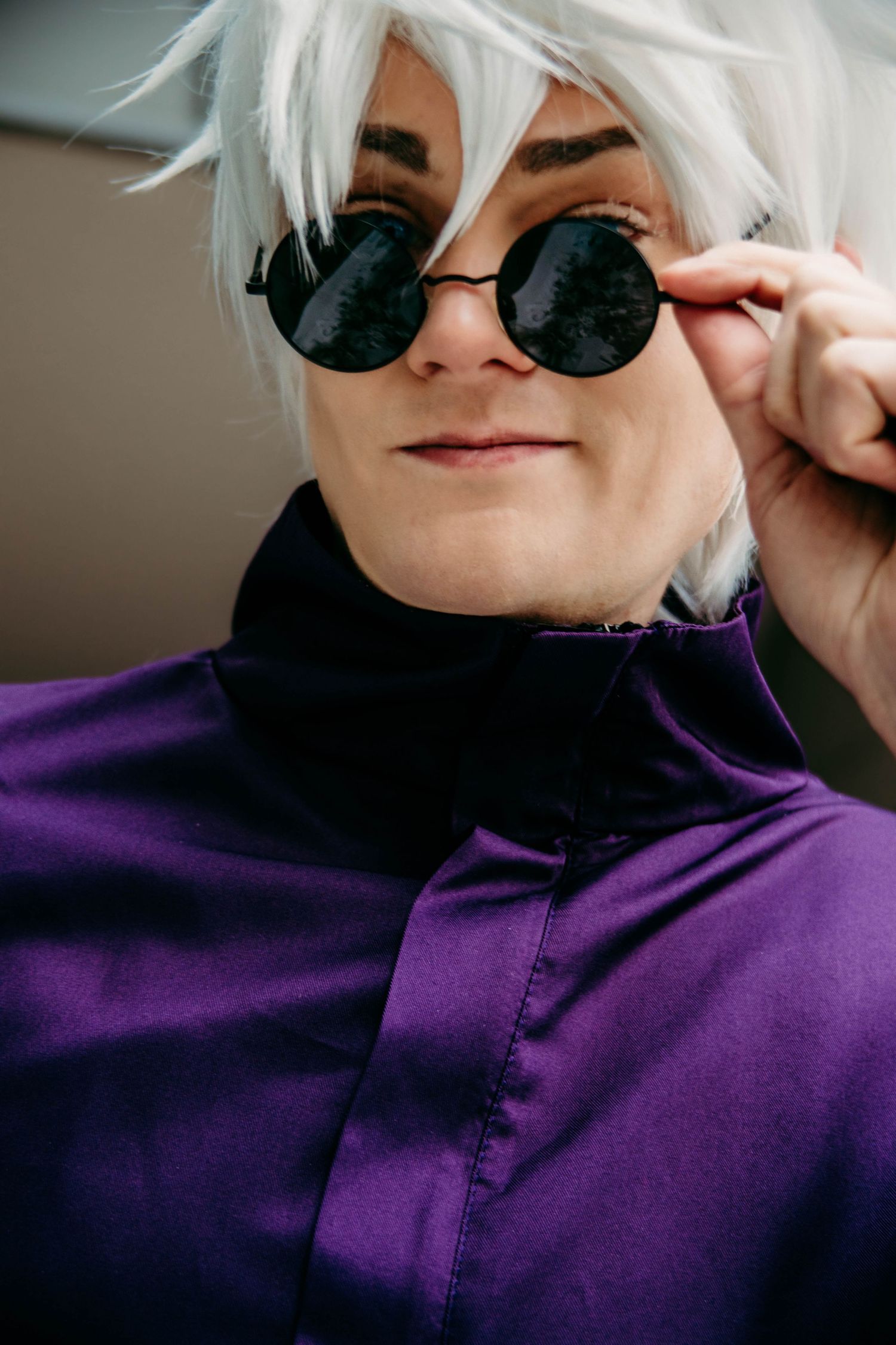 Close-up of cosplay character wearing round sunglasses and a purple high-neck jacket with spiky white hair.
