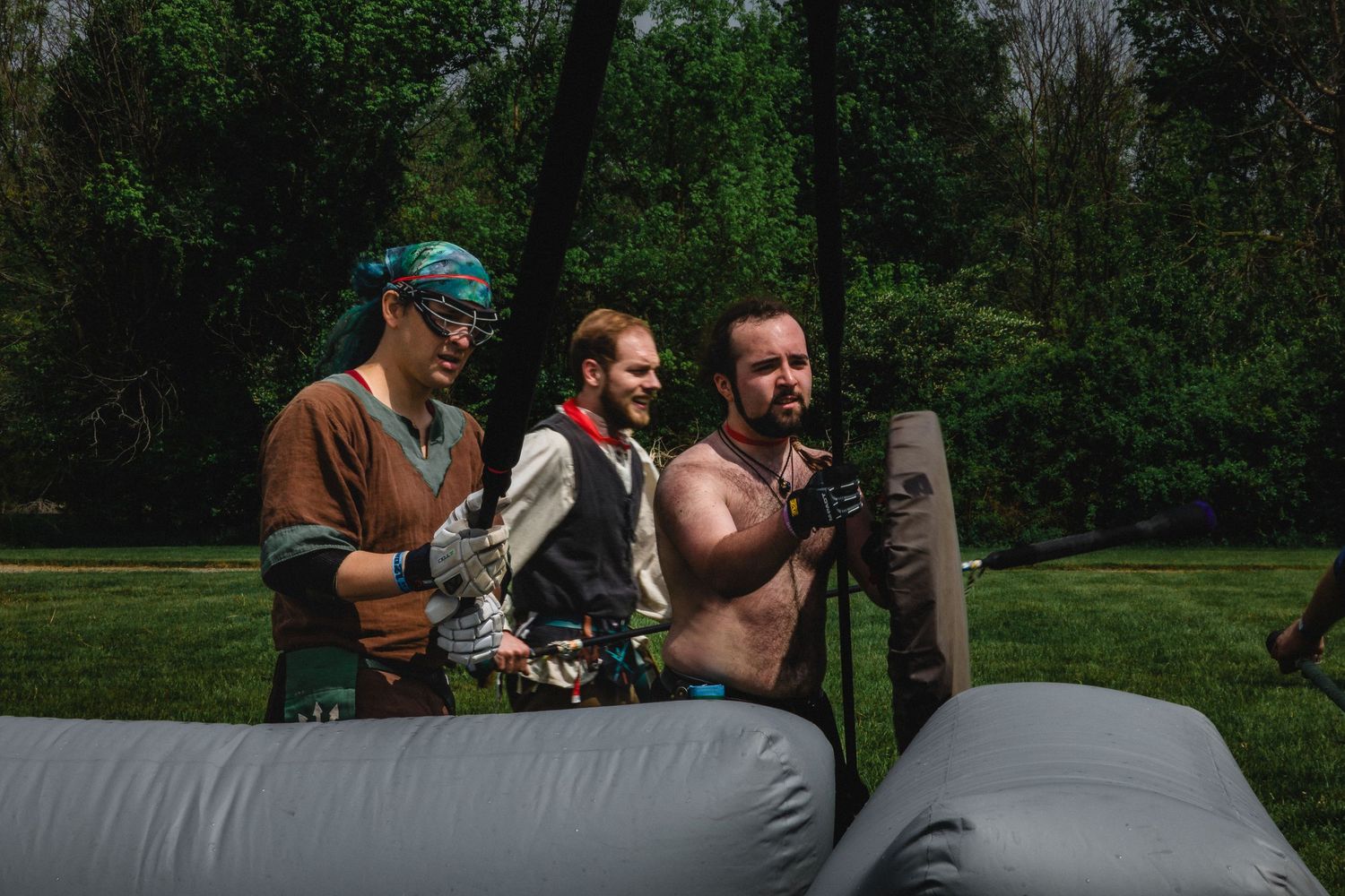 Three people in costumes stand near inflatable equipment in a lush green park setting.
