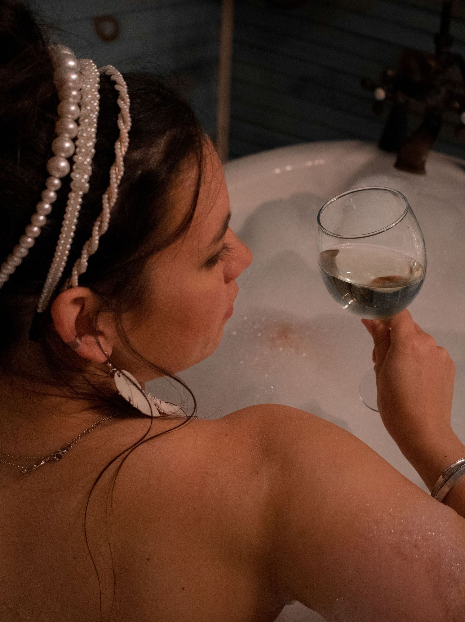 Relaxing bath scene with pearl hair accessories and wine glass.