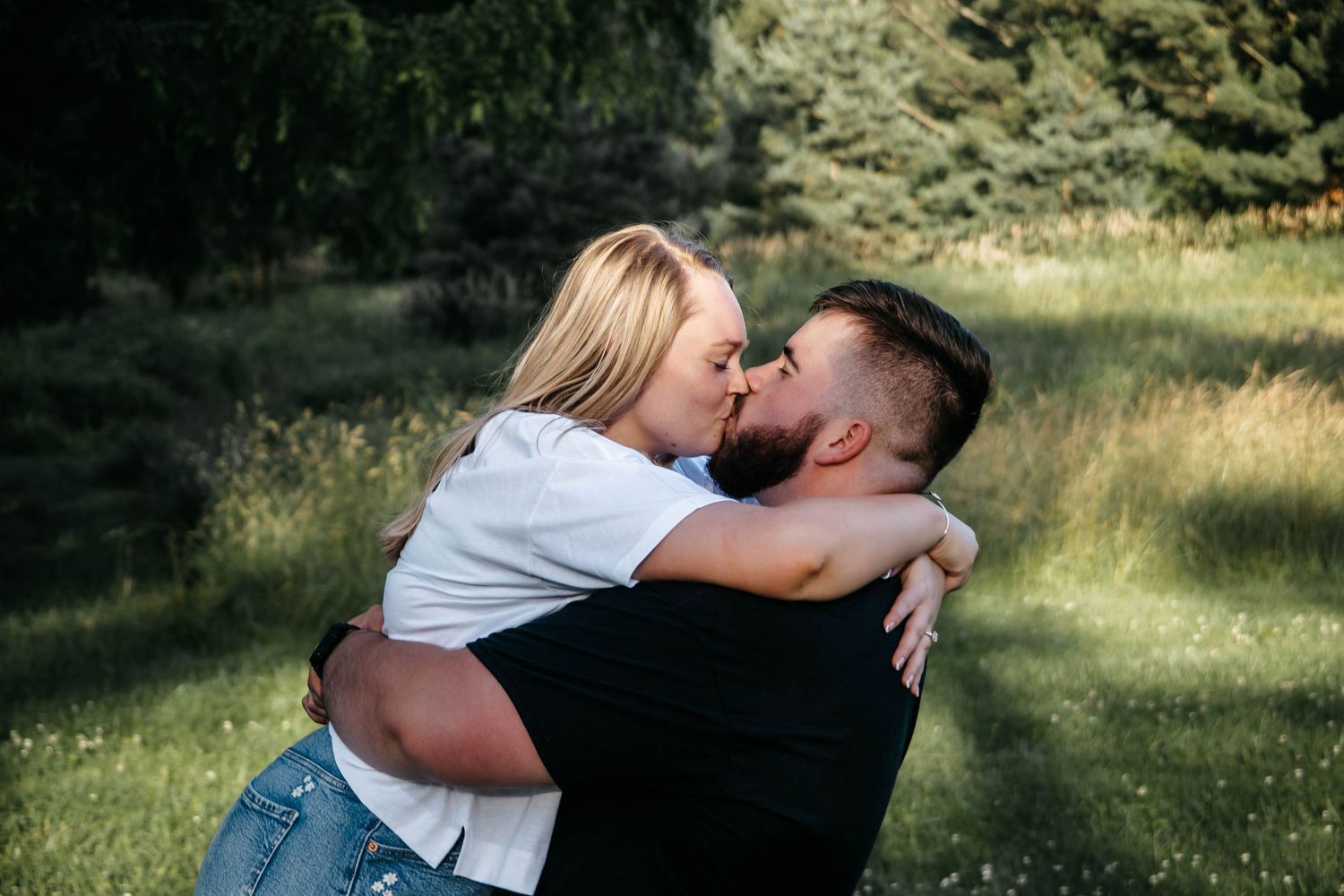 Romantic outdoor photoshoot with a couple embracing in a sunny natural setting.