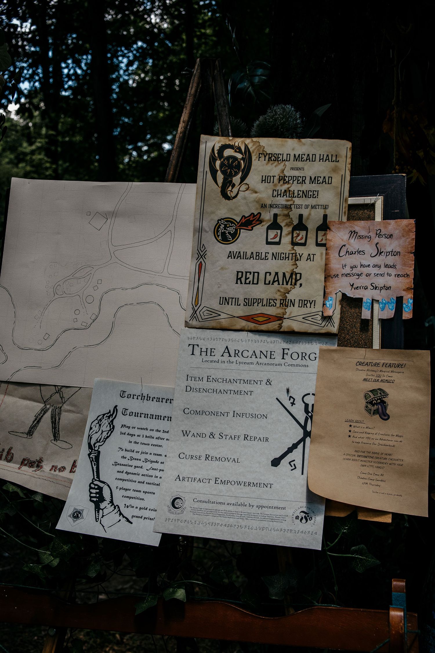 Fantasy LARP camp bulletin board displaying Arcane Forge services, Torchbearer Tournament, and Red Camp mead hall challenge flyers.