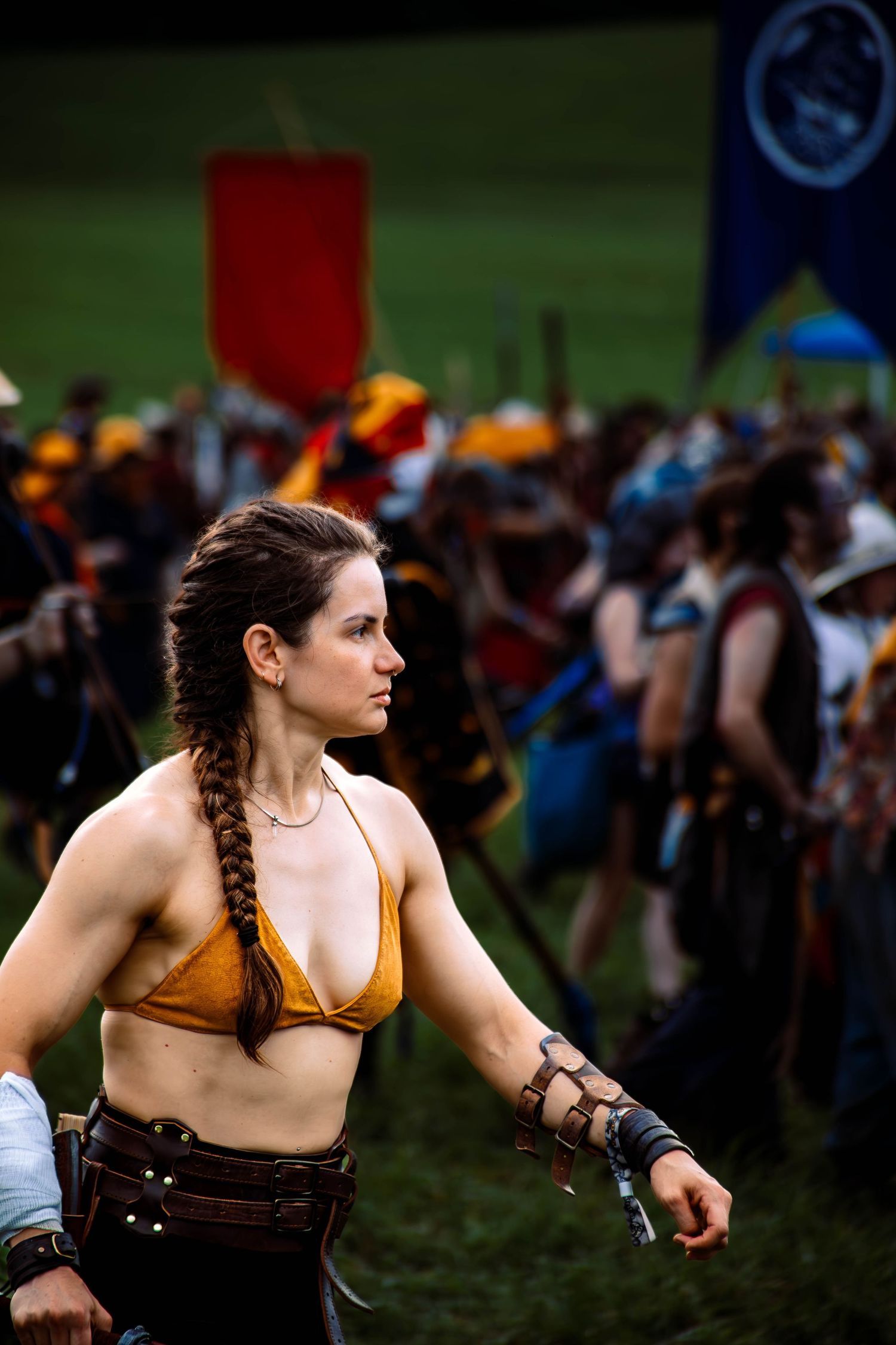 A woman in medieval costume armor performs combat moves at an outdoor renaissance festival.