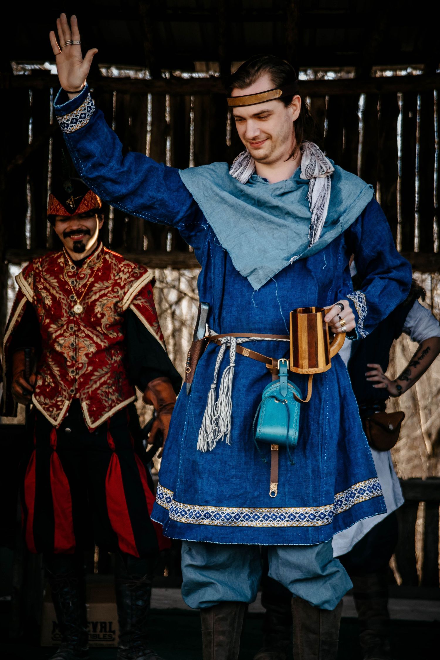Medieval performers in traditional period costumes pose during a historical reenactment, with one wearing bright blue attire.