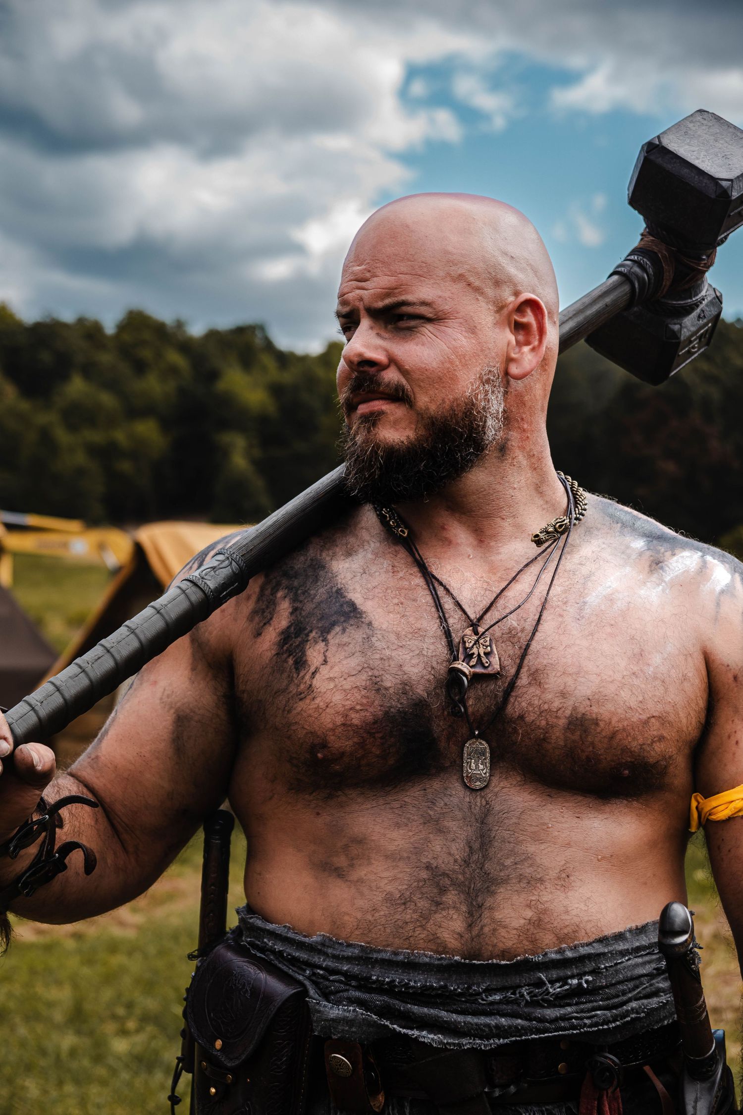 A shirtless warrior with a beard and tattoos poses dramatically with a weapon in a grassy field.