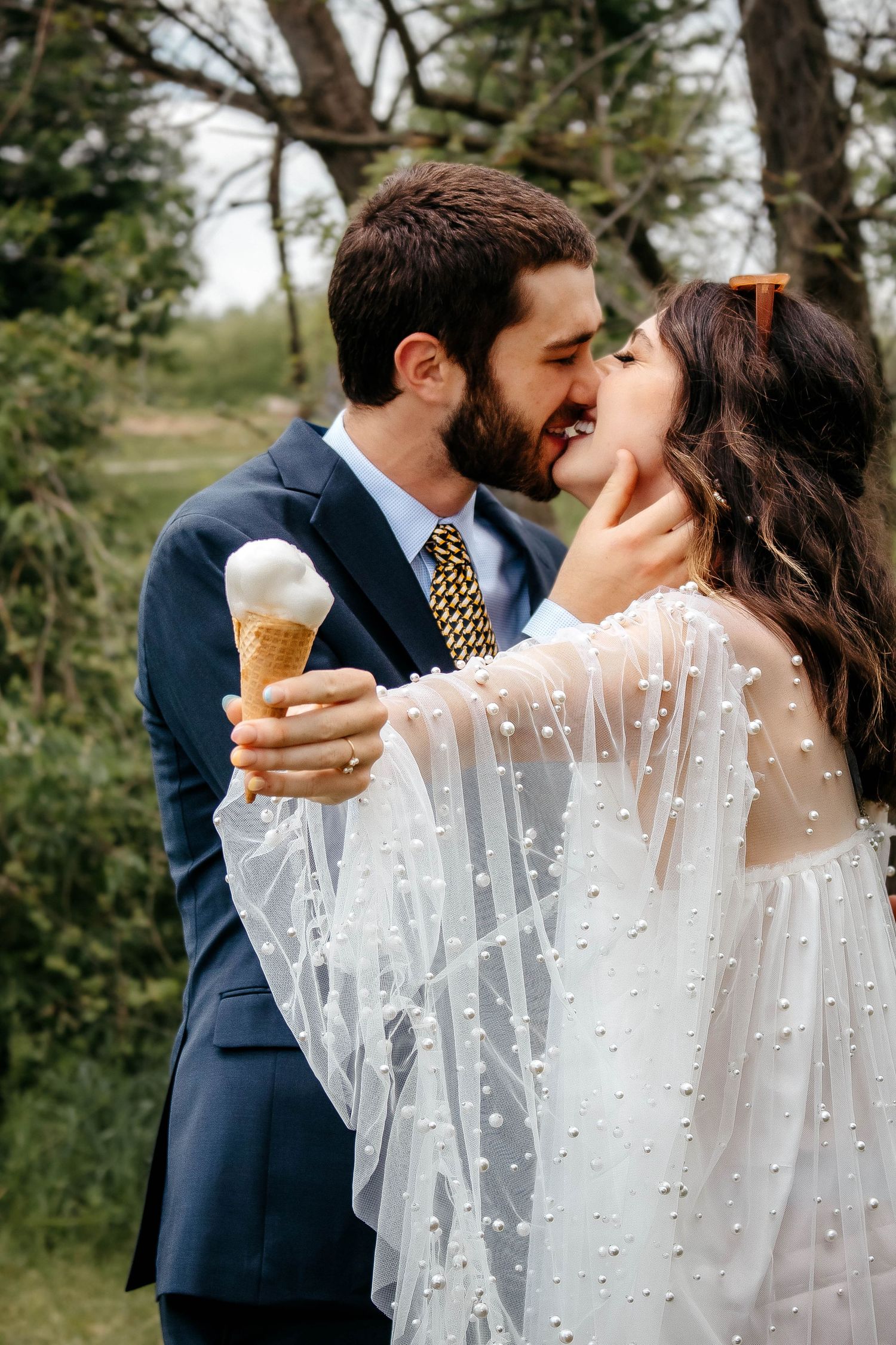 Couple sharing ice cream cones while bride wears delicate pearl-dotted veil.