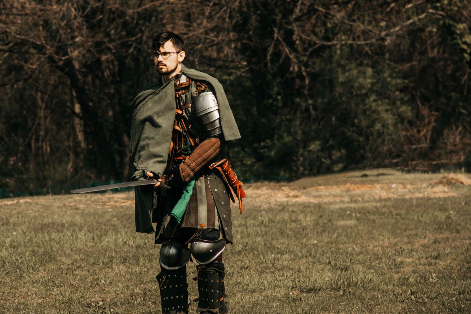 A hunter in camouflage gear walks through an autumn field carrying hunting equipment and a rifle.