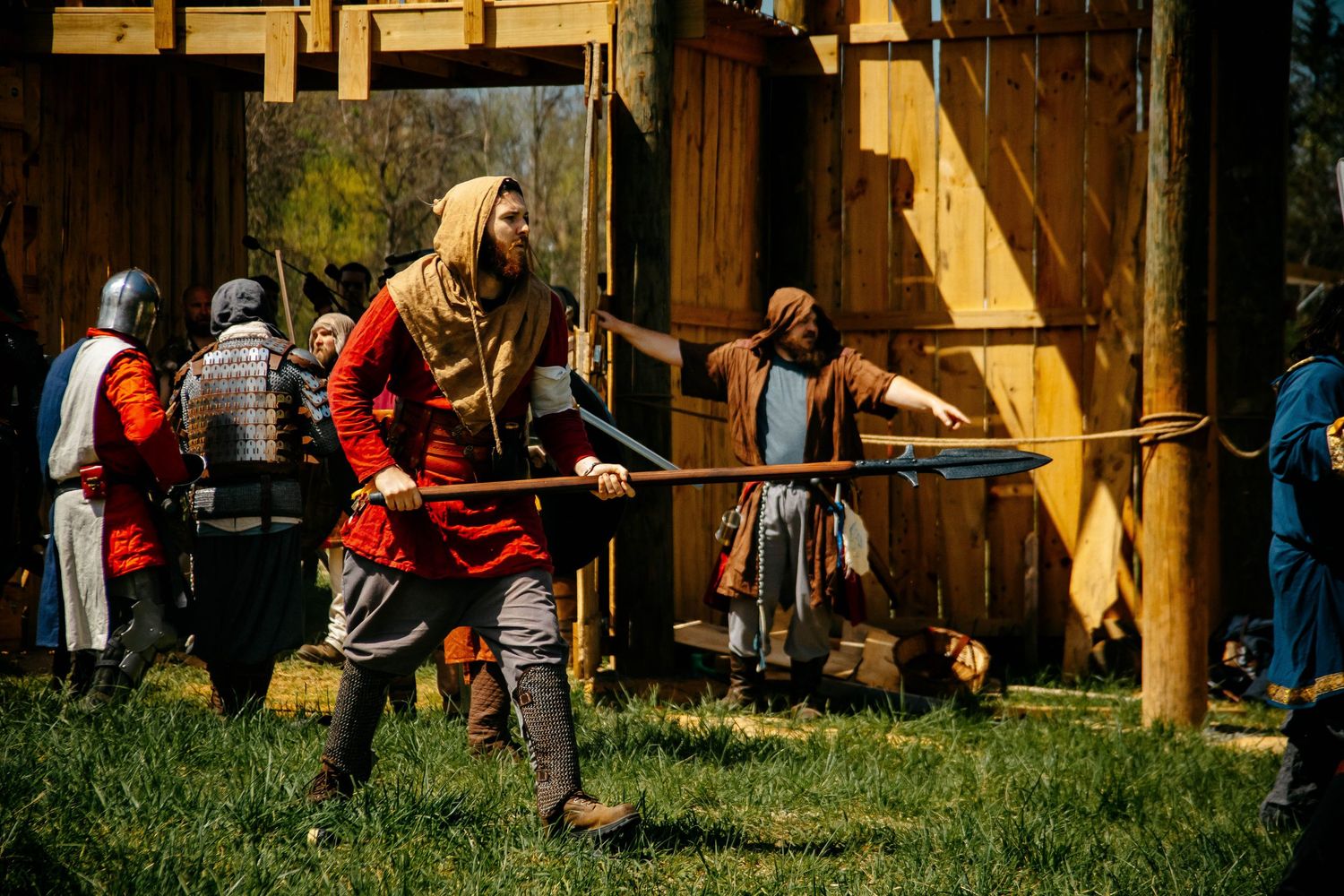 Medieval reenactors in period armor and clothing demonstrate combat techniques at an outdoor historical event.