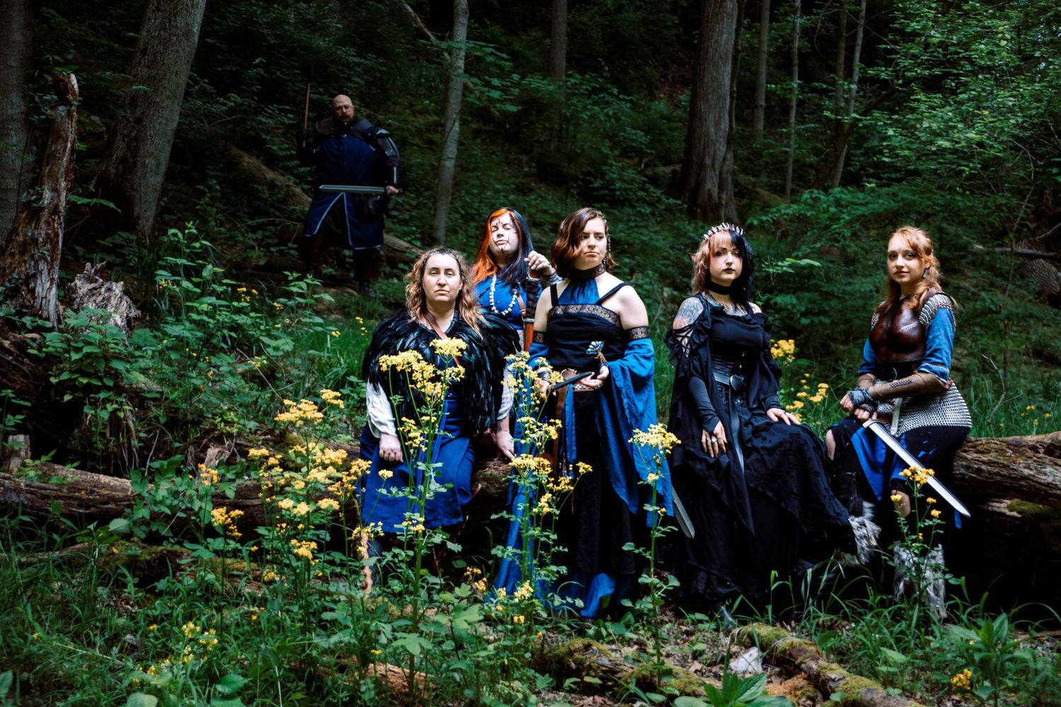 A group of people in blue jackets explore a lush forest trail with yellow wildflowers blooming along the path.