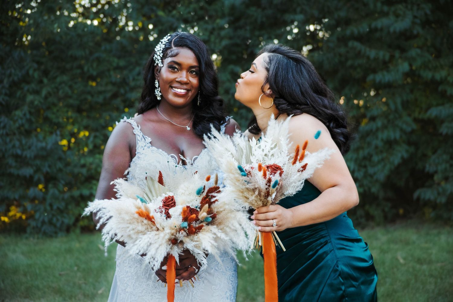 Two people in wedding attire laugh and embrace while holding bouquets in an outdoor garden setting at sunset.