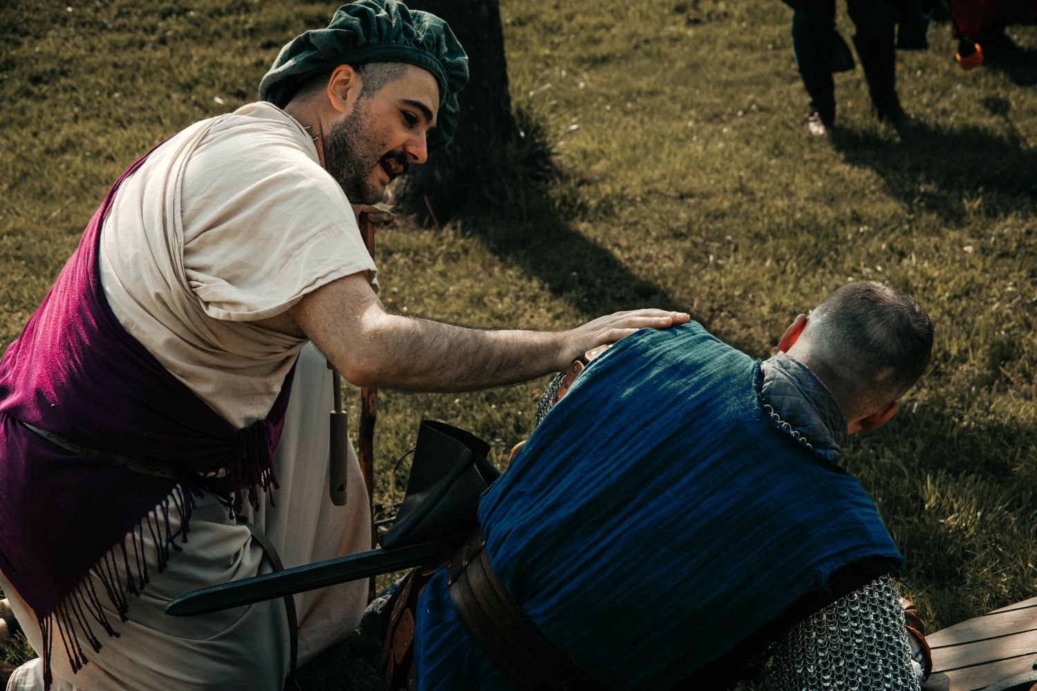 Two people engaged in a playful wrestling match on grass during an outdoor event.