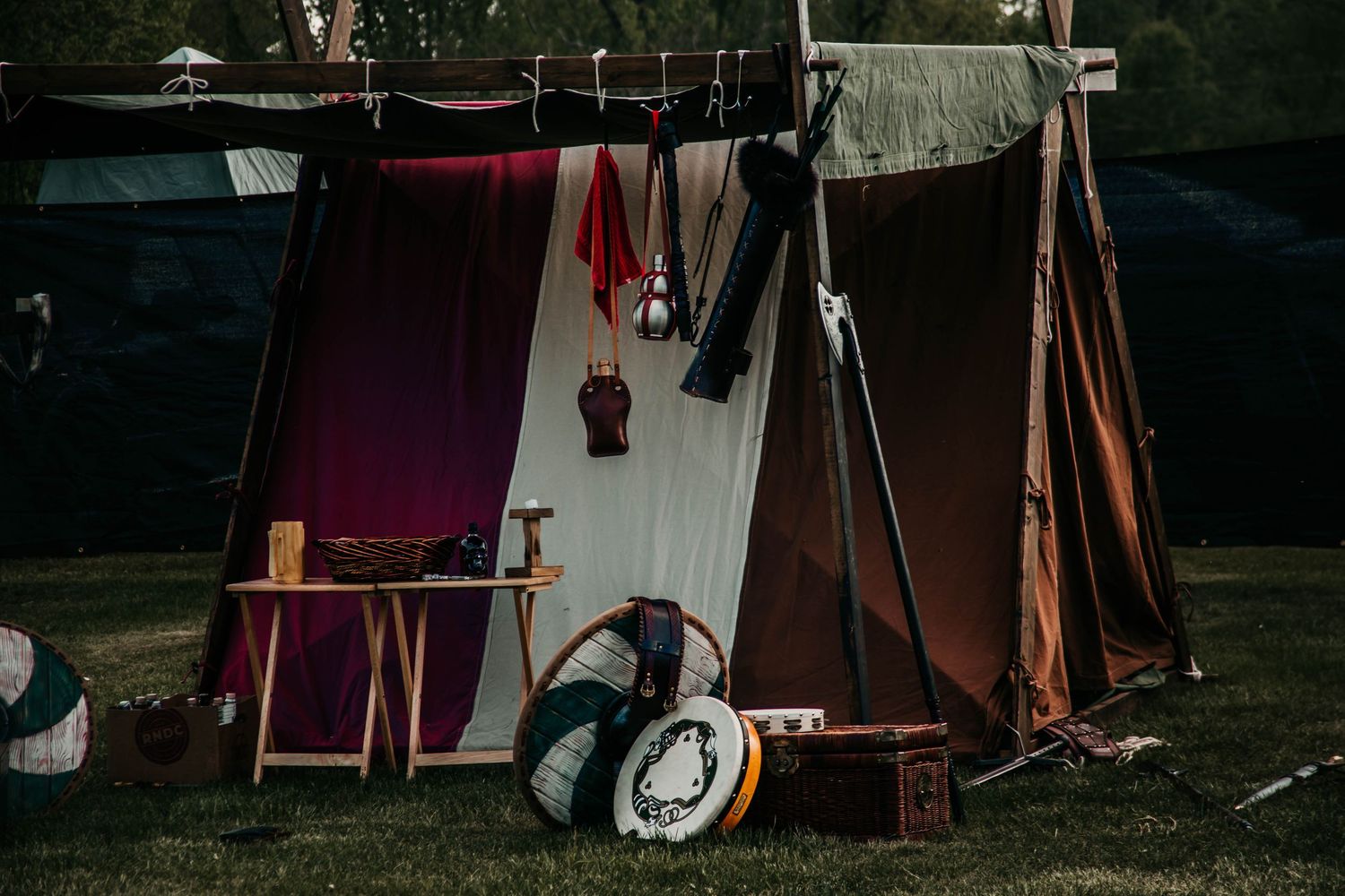 Medieval-style encampment with tents and banners set up in a wooded area during a historical reenactment event.