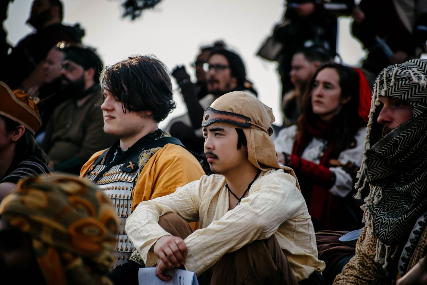 A crowd of medieval reenactors in period costumes gather outdoors during a historical festival.