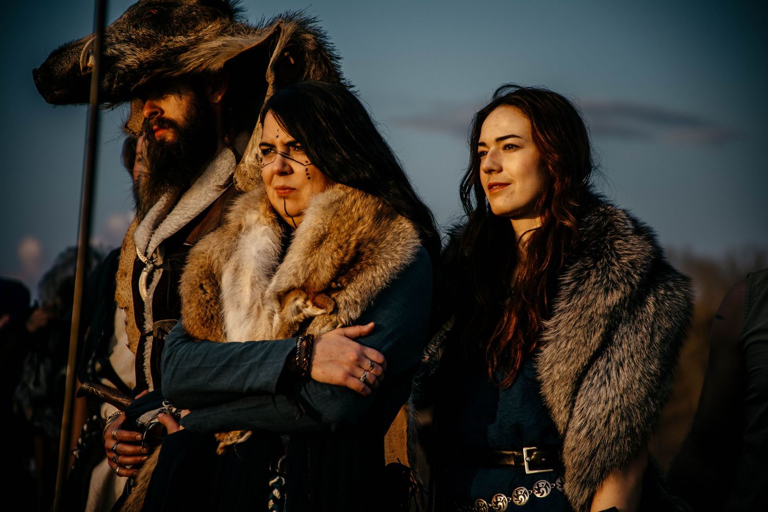 A couple in winter coats embraces at sunset while standing outdoors in golden light.