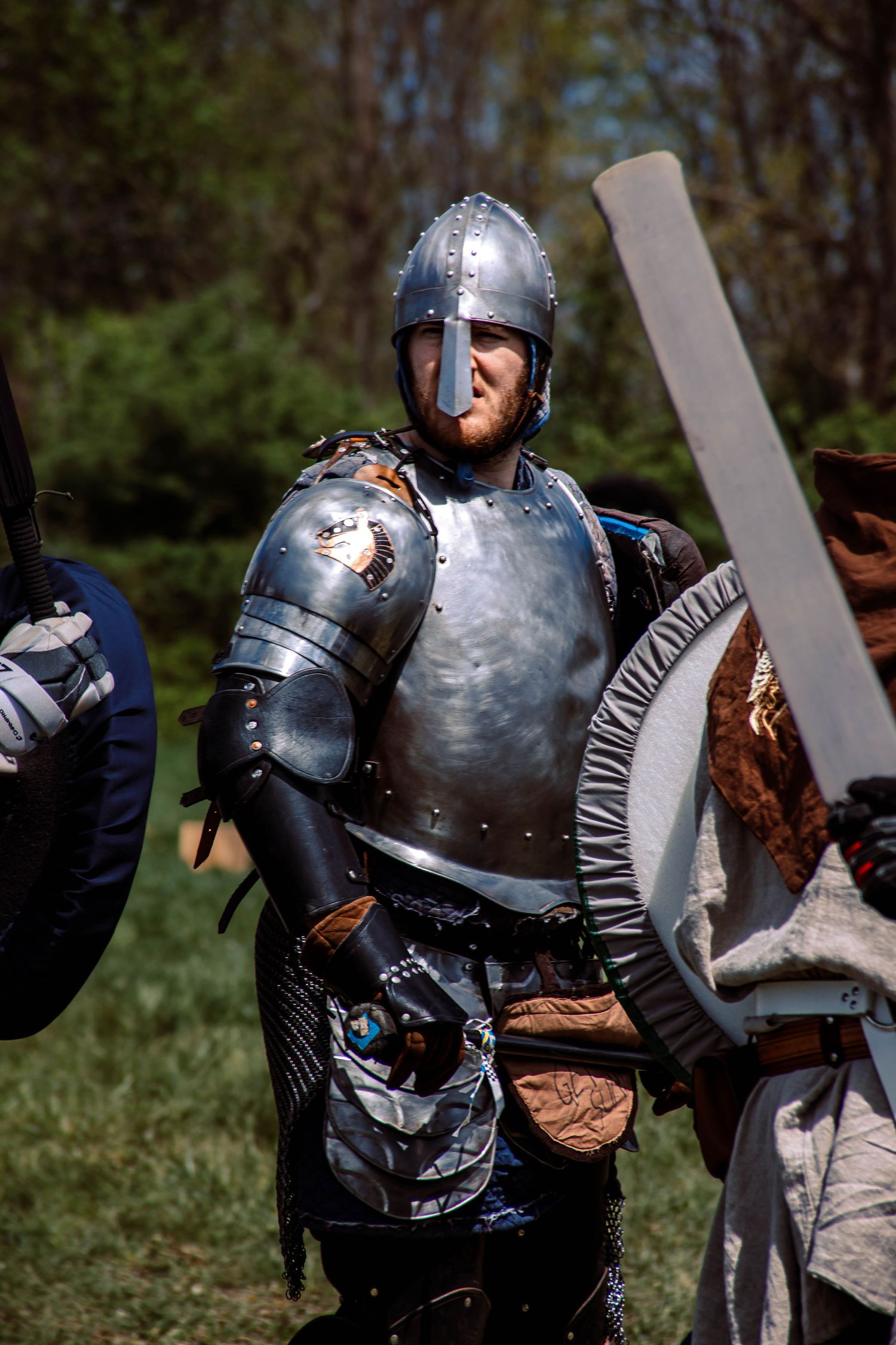 Medieval knight in shining armor practicing sword combat techniques with a training partner in an outdoor setting.