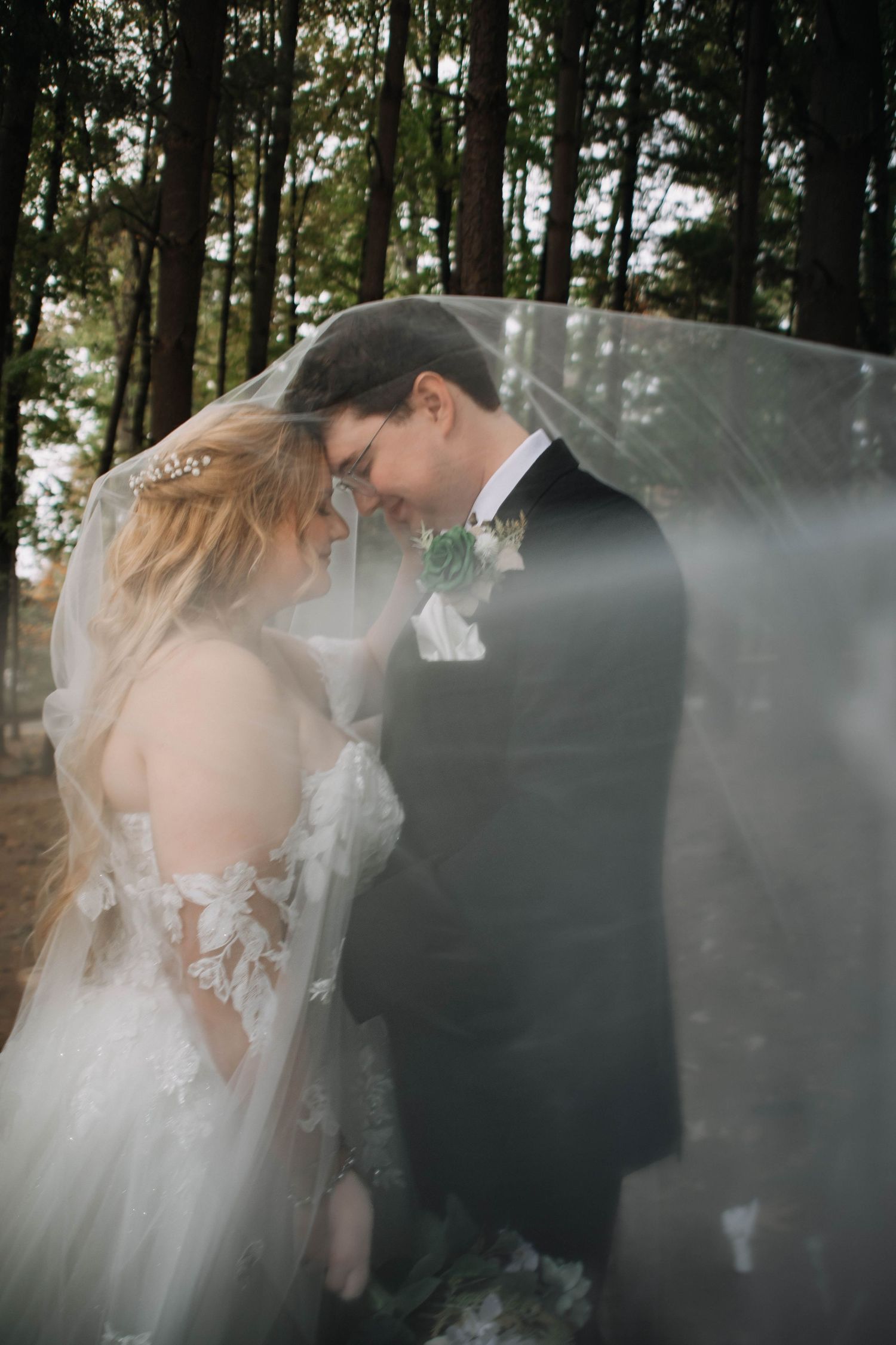 Romantic wedding couple embraces in a misty forest setting with ethereal veil movement creating a dreamy atmosphere.