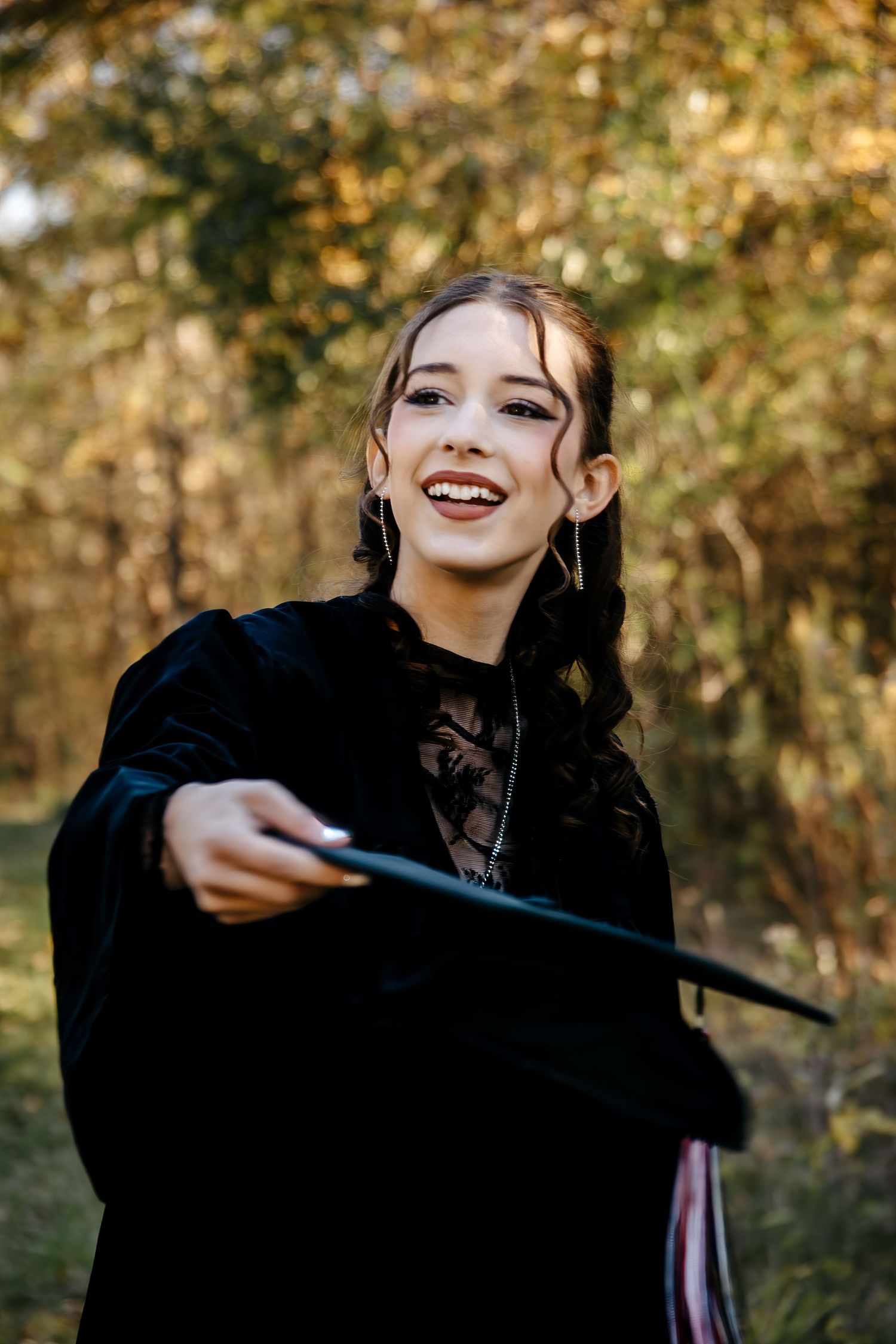 A person in black clothing laughs joyfully while posing in an outdoor autumn setting.