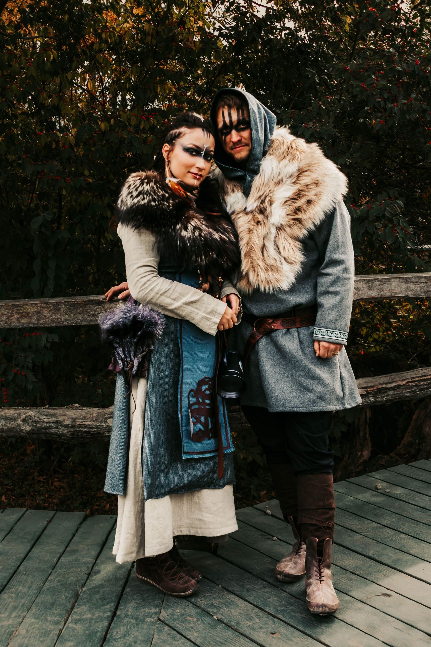 Two people in winter coats embrace on a wooden deck during an autumn photoshoot.