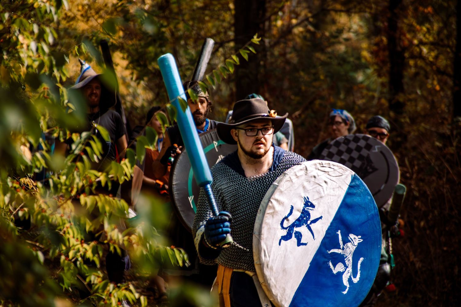 Medieval knight in blue tunic with lion emblem practices sword fighting techniques in autumn forest setting.