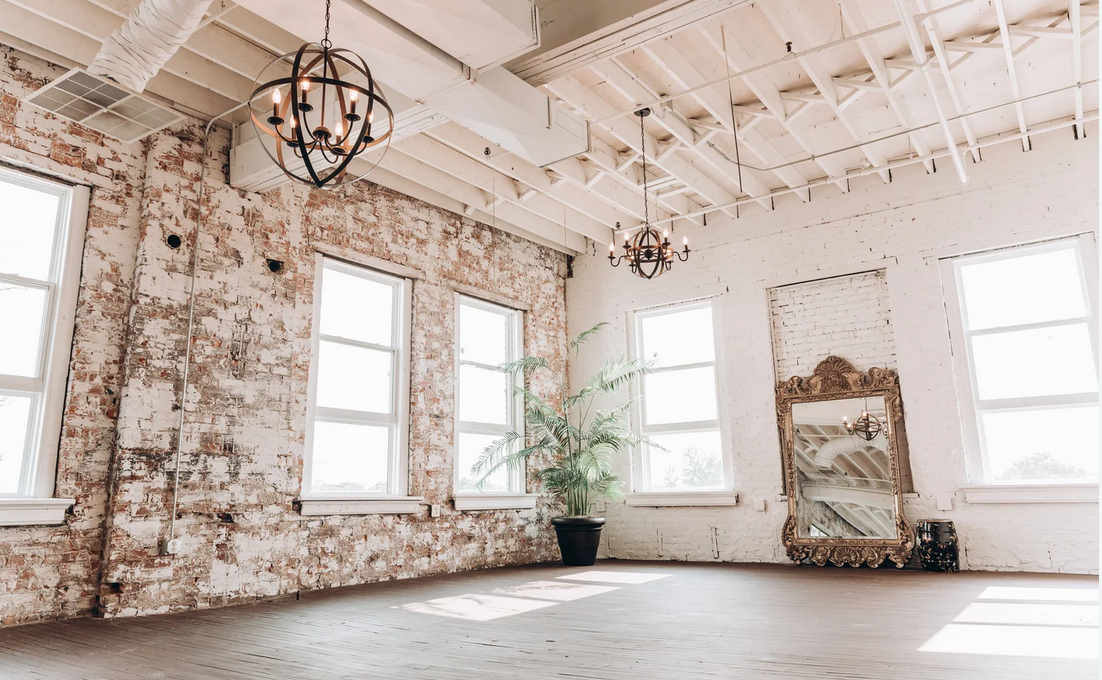 Bright rustic studio space with exposed brick walls, vintage mirror, hanging lanterns and large windows.