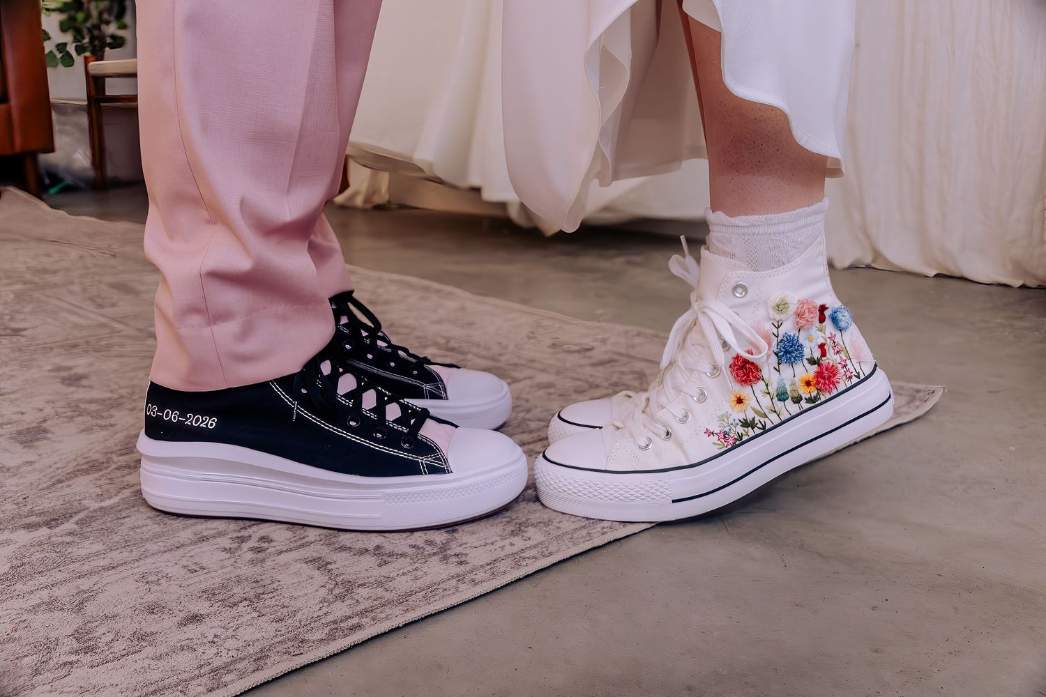 Bride and groom wearing matching Converse sneakers, white floral high-tops and black low-tops, at wedding.