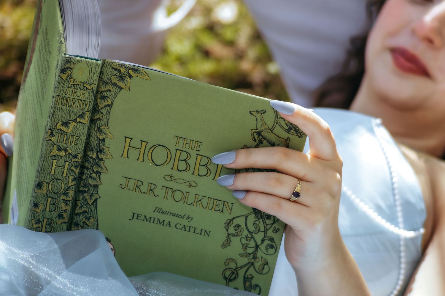 Woman in white dress reading a green hardcover edition of The Hobbit by J.R.R. Tolkien illustrated by Jemima Catlin.