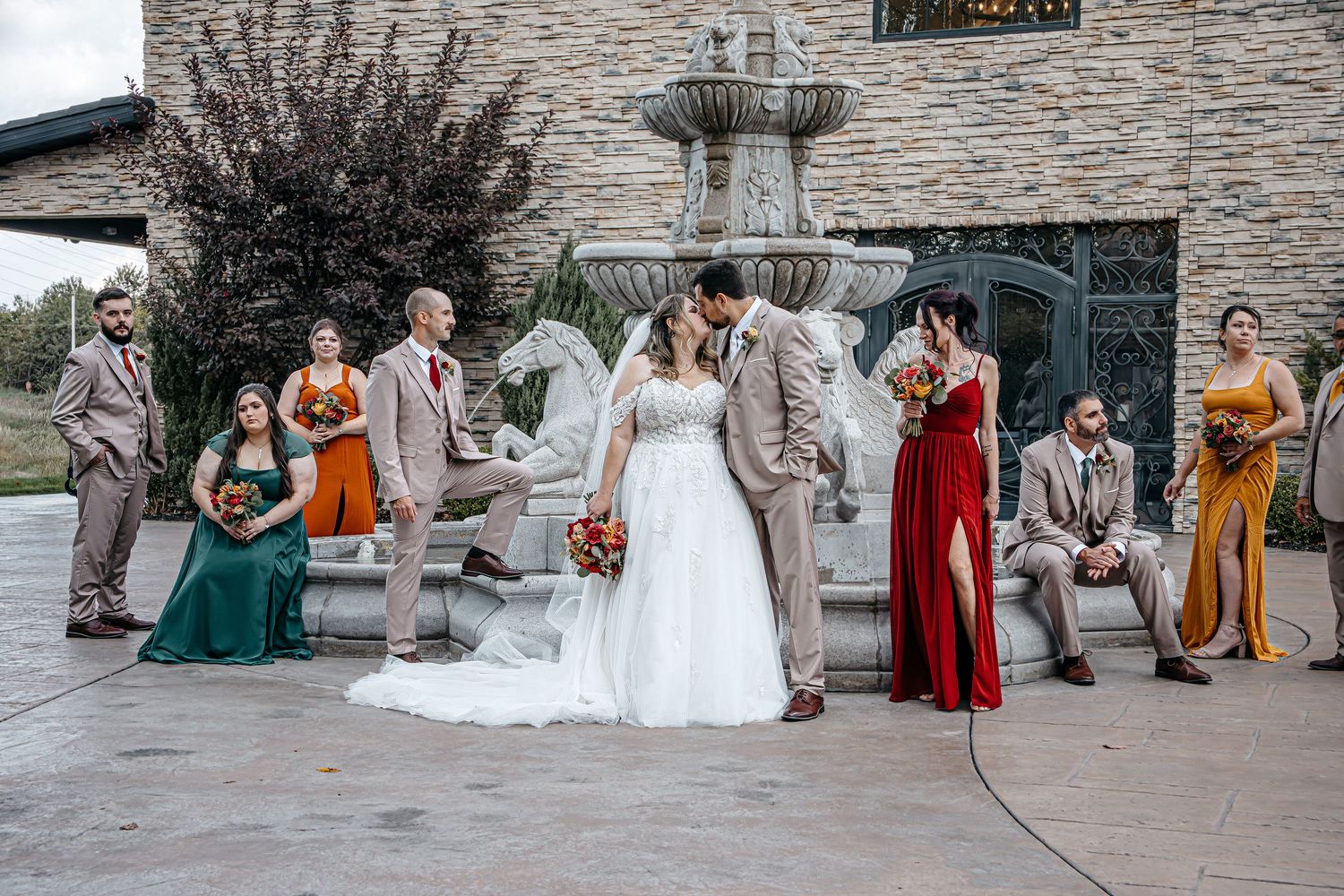 Wedding party in colorful burgundy and mustard dresses poses together on stone patio during autumn celebration.