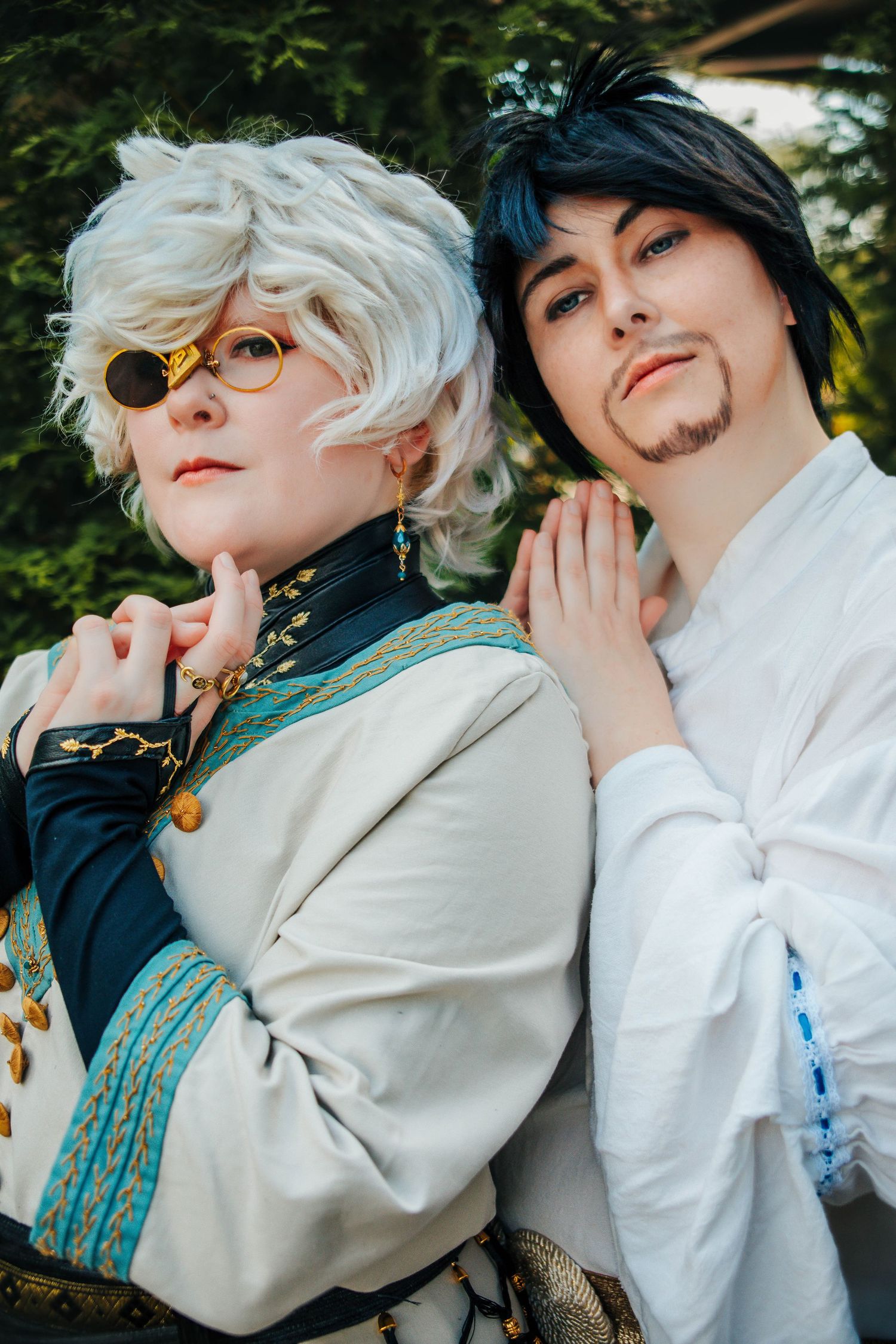 Two cosplayers pose together in white and beige outfits with steampunk-inspired accessories and goggles.