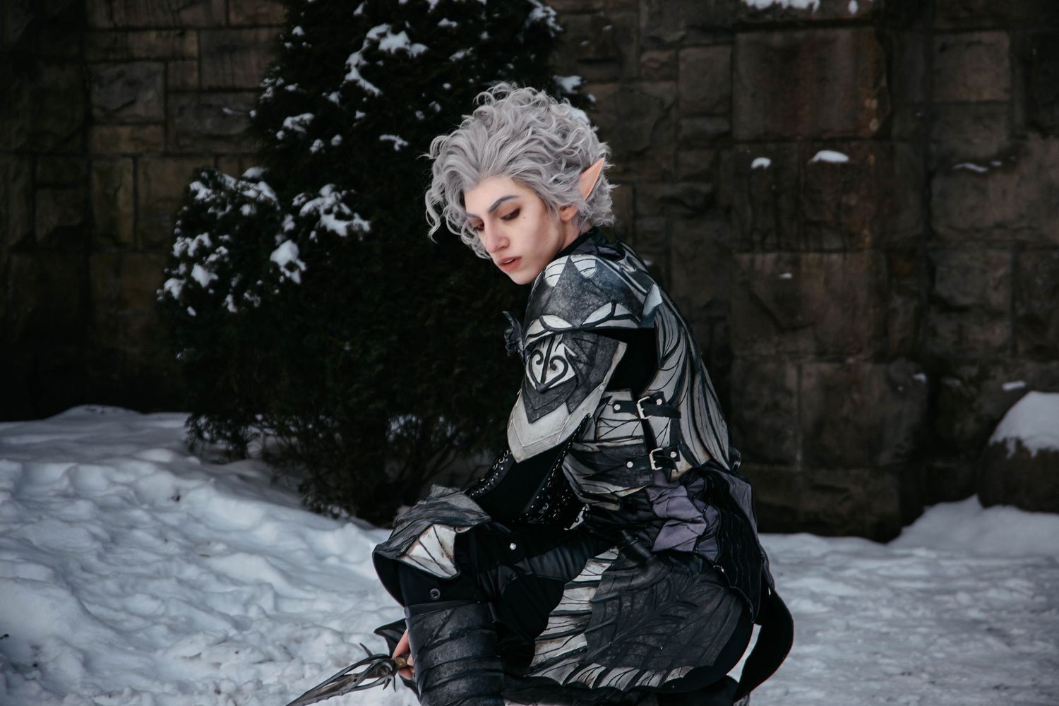 Winter fantasy cosplay shoot with dark costume against snowy stone backdrop.