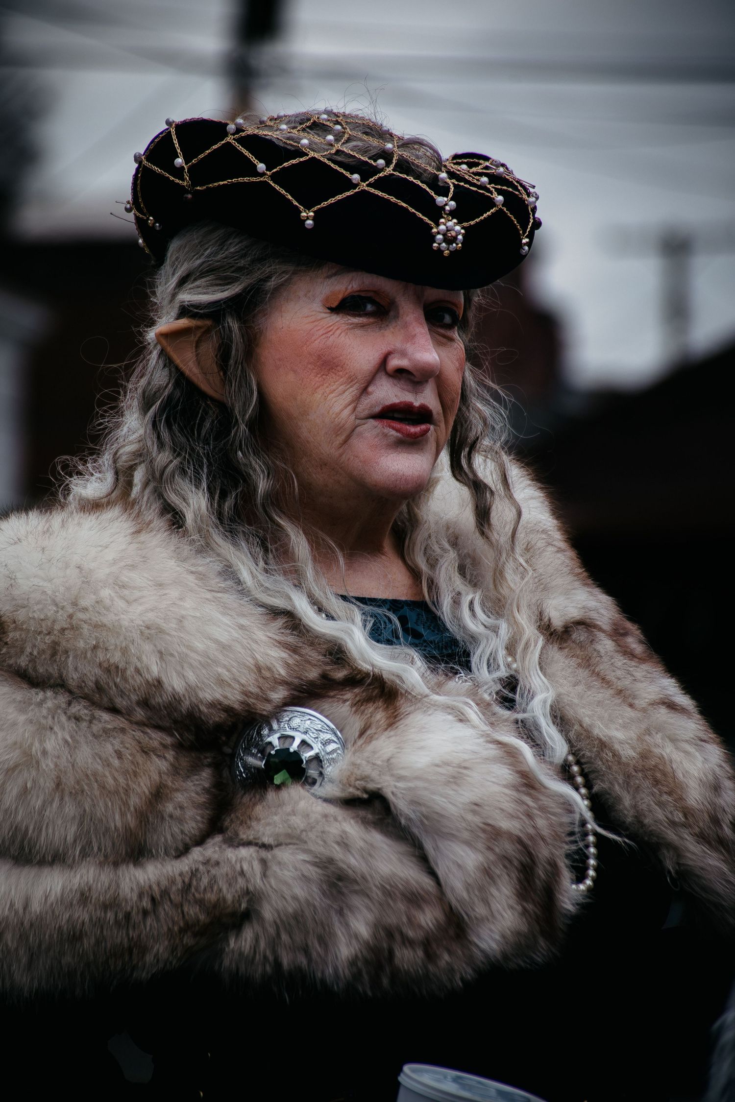 Woman in medieval attire with fur collar and ornate headpiece at renaissance festival.