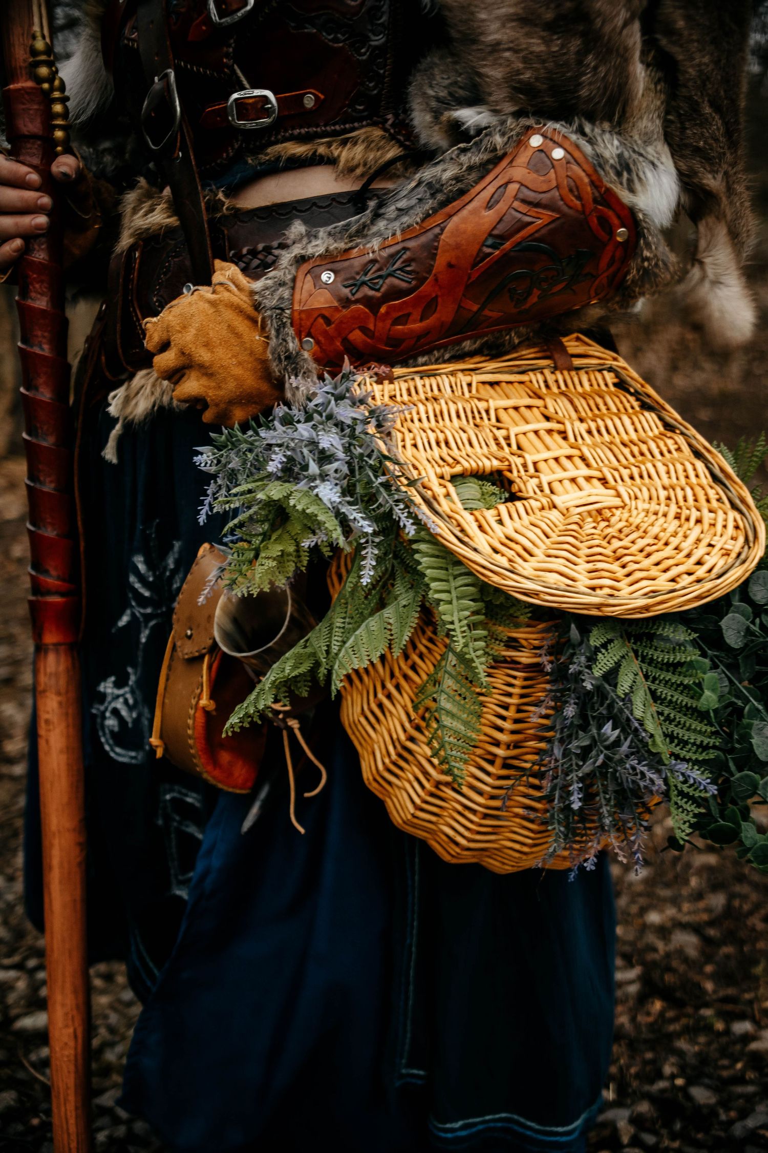 Rustic wicker baskets decorated with evergreen branches and feathers hang against a dark background with navy fabric.