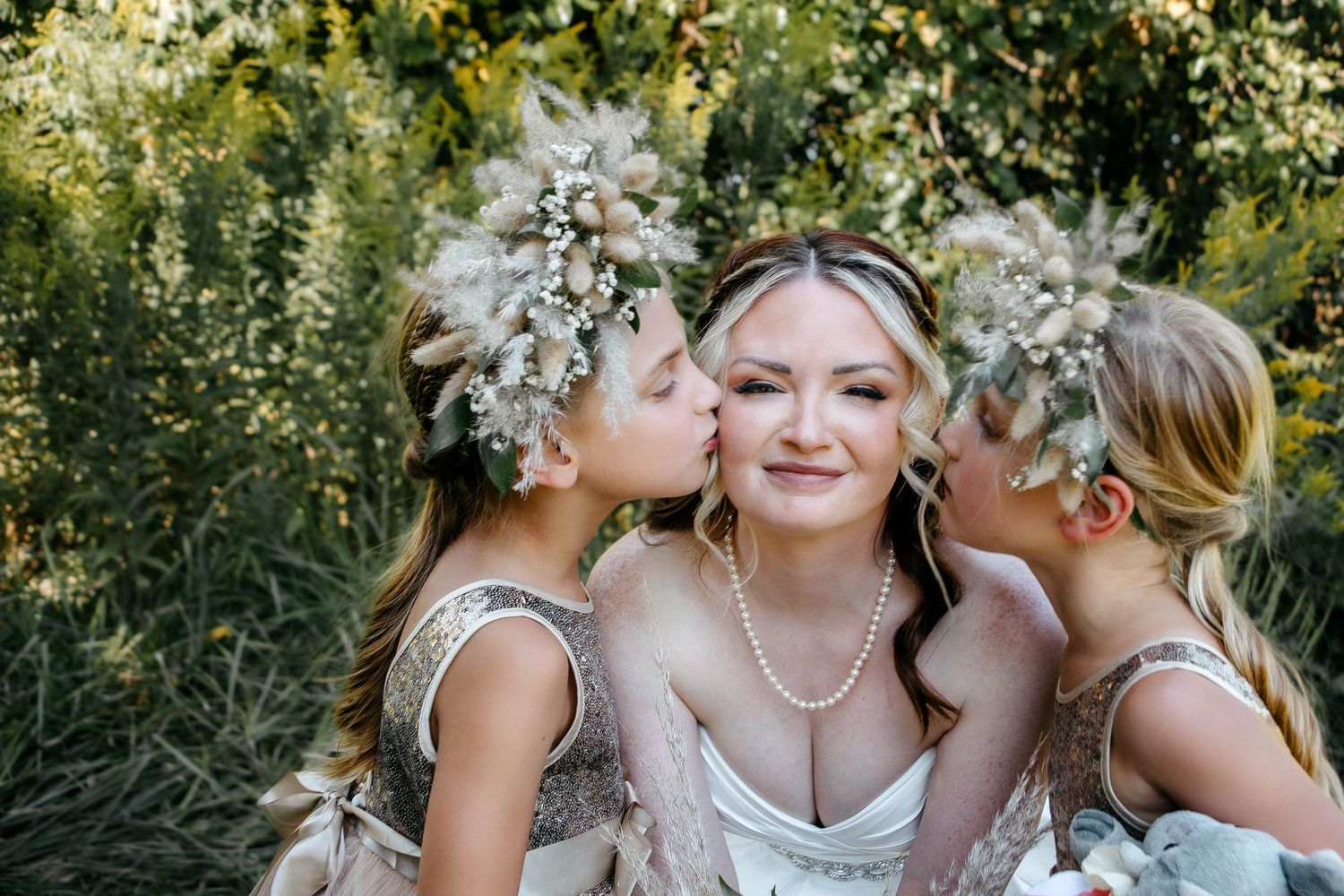 Bridesmaids wearing white dresses share tender moments with the bride while wearing delicate floral crowns in a garden setting.