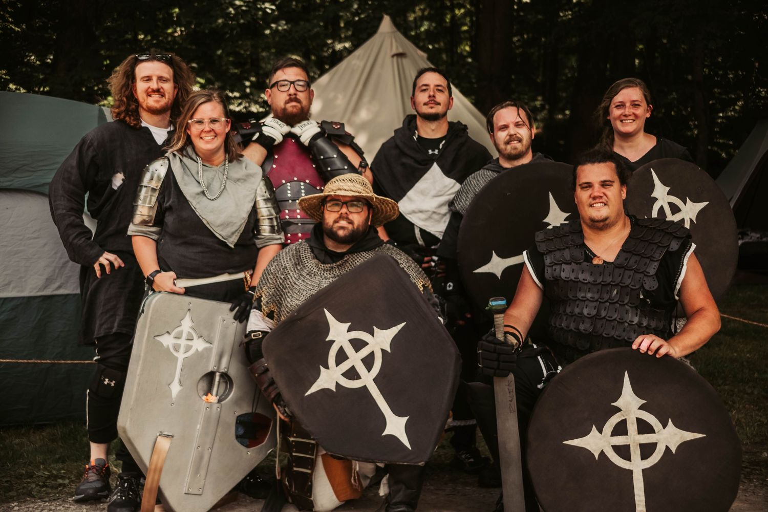 Group of people wearing black t-shirts with matching symbol designs gather together at an outdoor event.
