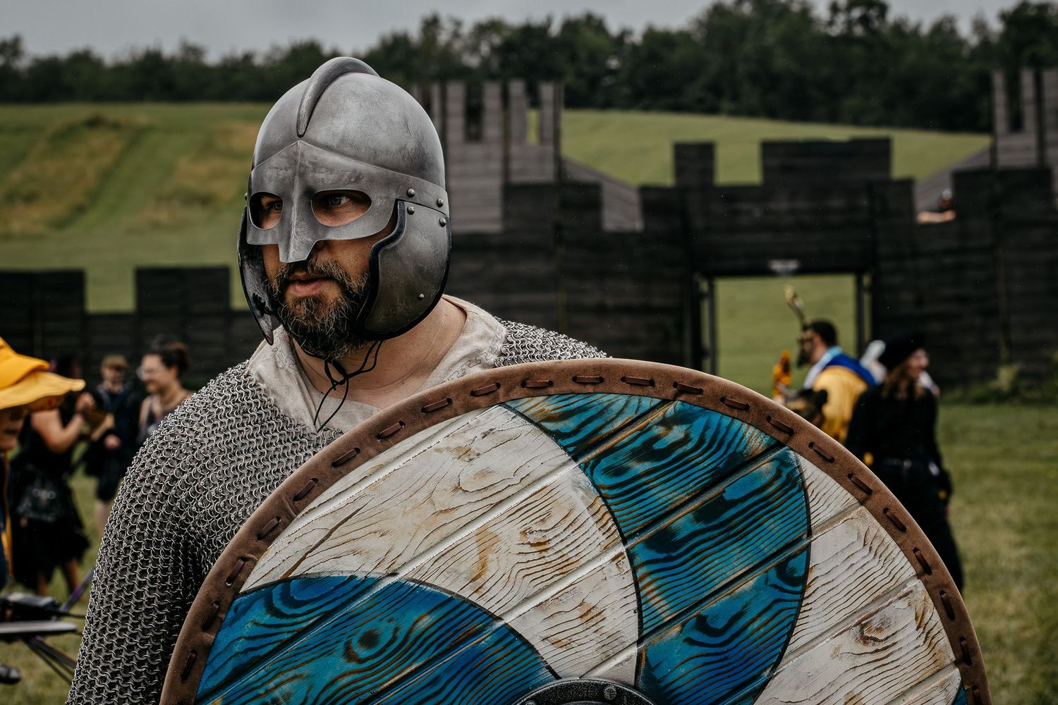 Medieval Viking warrior in chainmail armor and helmet holding a decorative round shield at historical reenactment event.