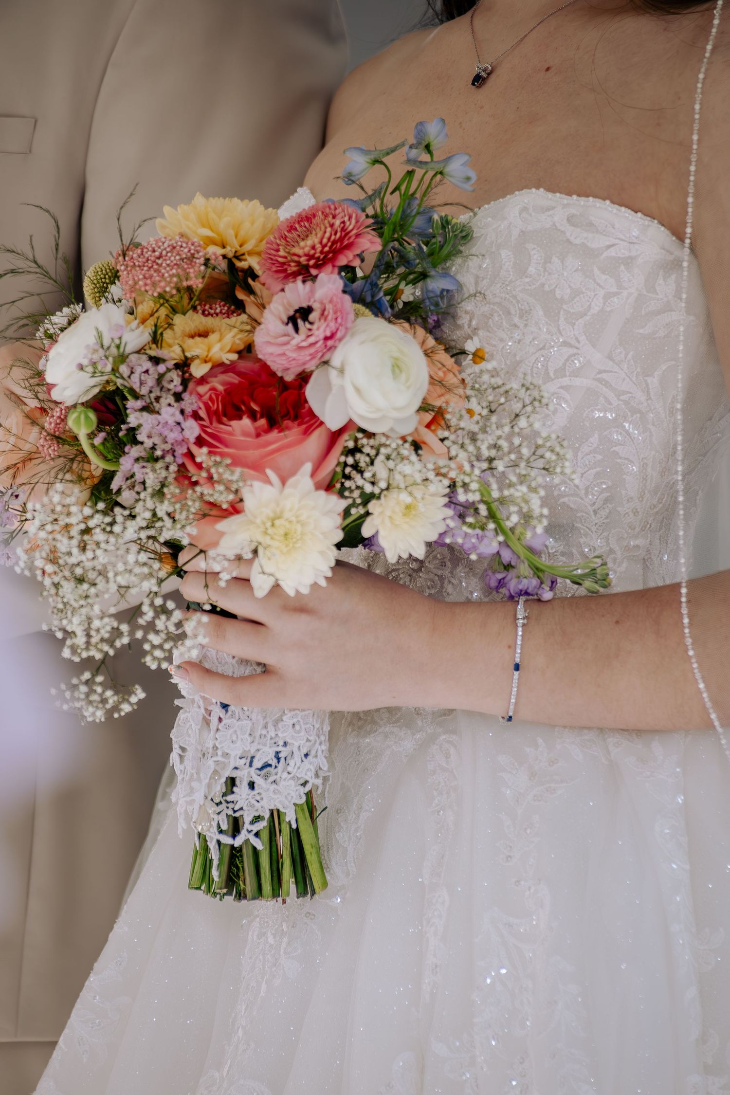 Bride in white lace gown holding colorful wedding bouquet with roses, ranunculus, and baby's breath.