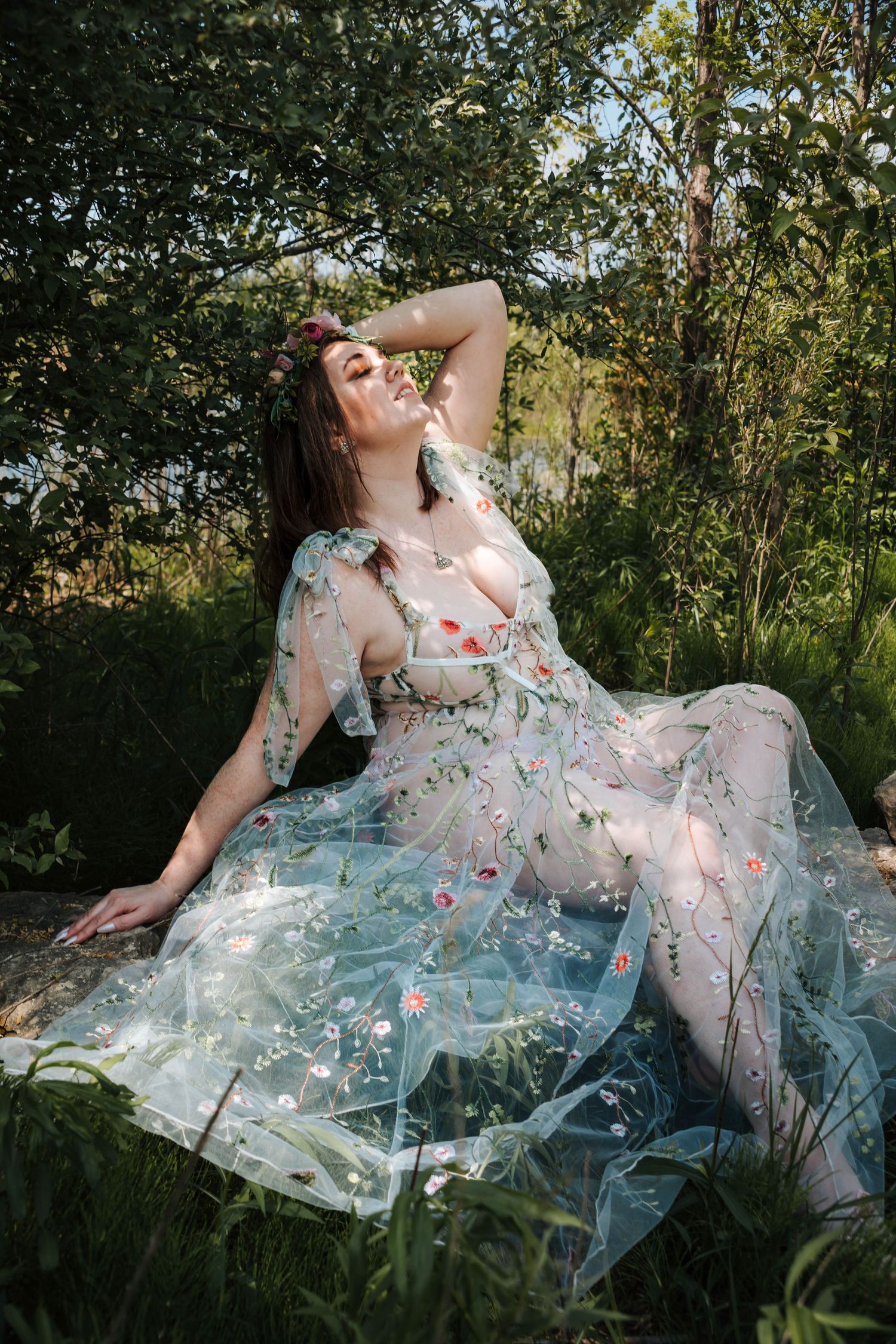 A sheer floral dress with delicate embroidery flows gracefully across green grass in a garden setting.