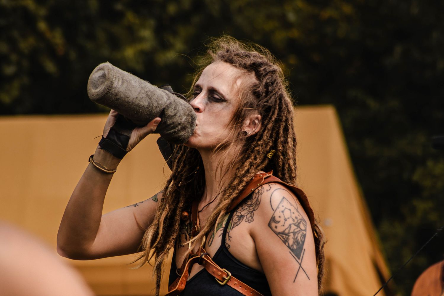 Performer on stage with tattoos and long hair drinks from a water bottle during a live music performance.