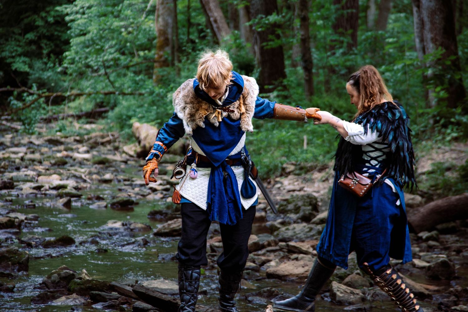 People in dark clothing practice combat moves in a wooded forest setting.