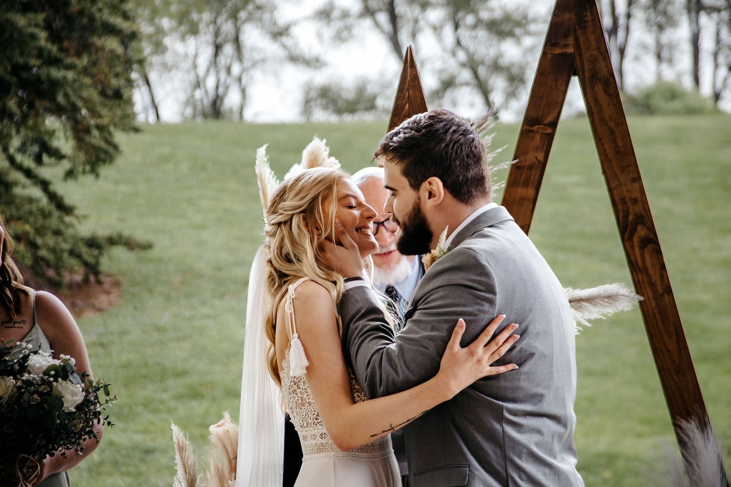A romantic wedding kiss moment captured under a wooden triangular arch in an outdoor garden setting.
