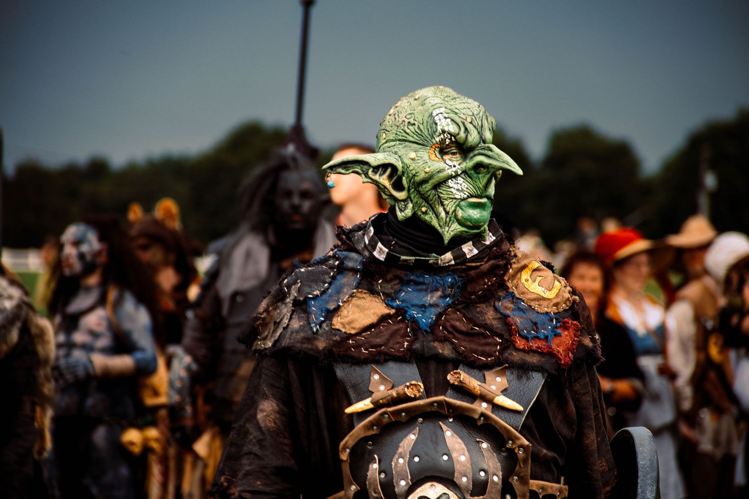 A crowd of people wearing costumes and masks gather at an outdoor event in dark lighting.
