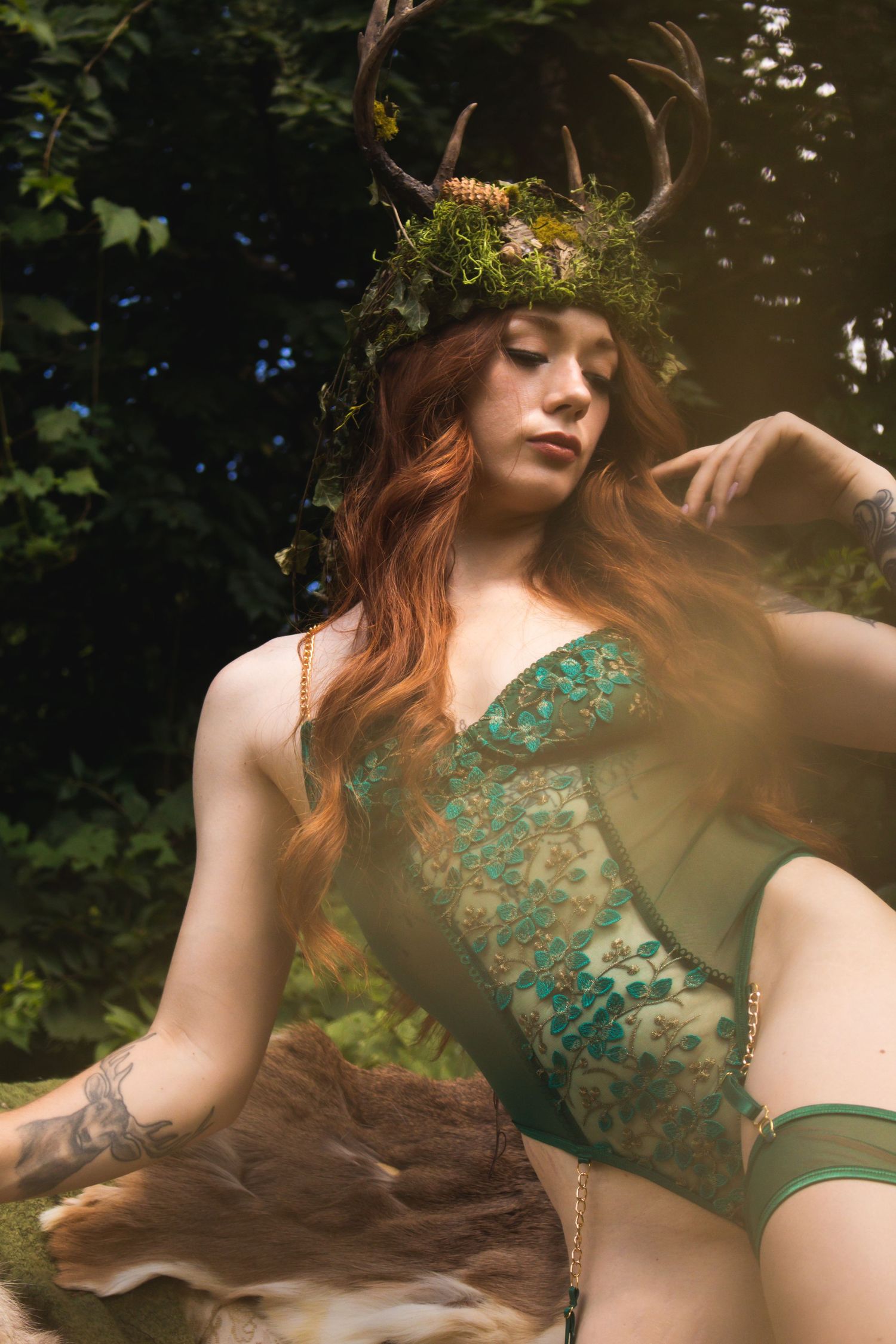 Ethereal forest photoshoot featuring a green lace bodysuit and antler crown with natural woodland elements.