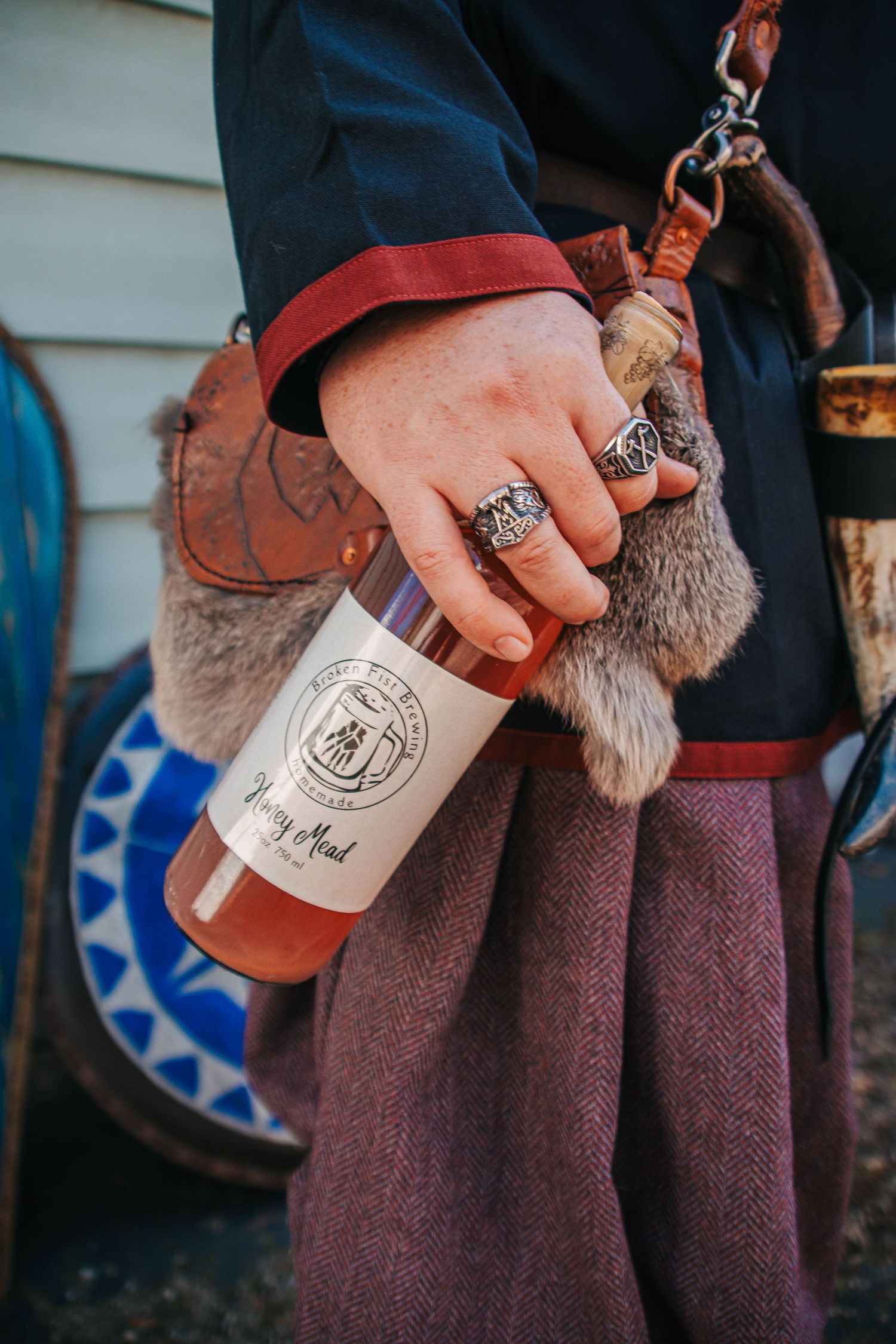 Close-up sequence of hands holding a bottle of artisanal spirits against a textured burgundy fabric background.