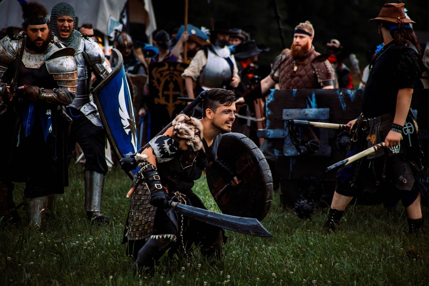 Medieval costumed performers engage in combat roleplay on grassy field during a live action event.